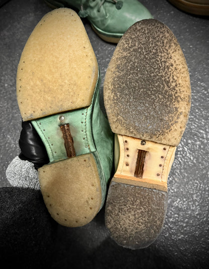 Close-up of worn-out shoe soles with visible wear and tear on a dark surface.