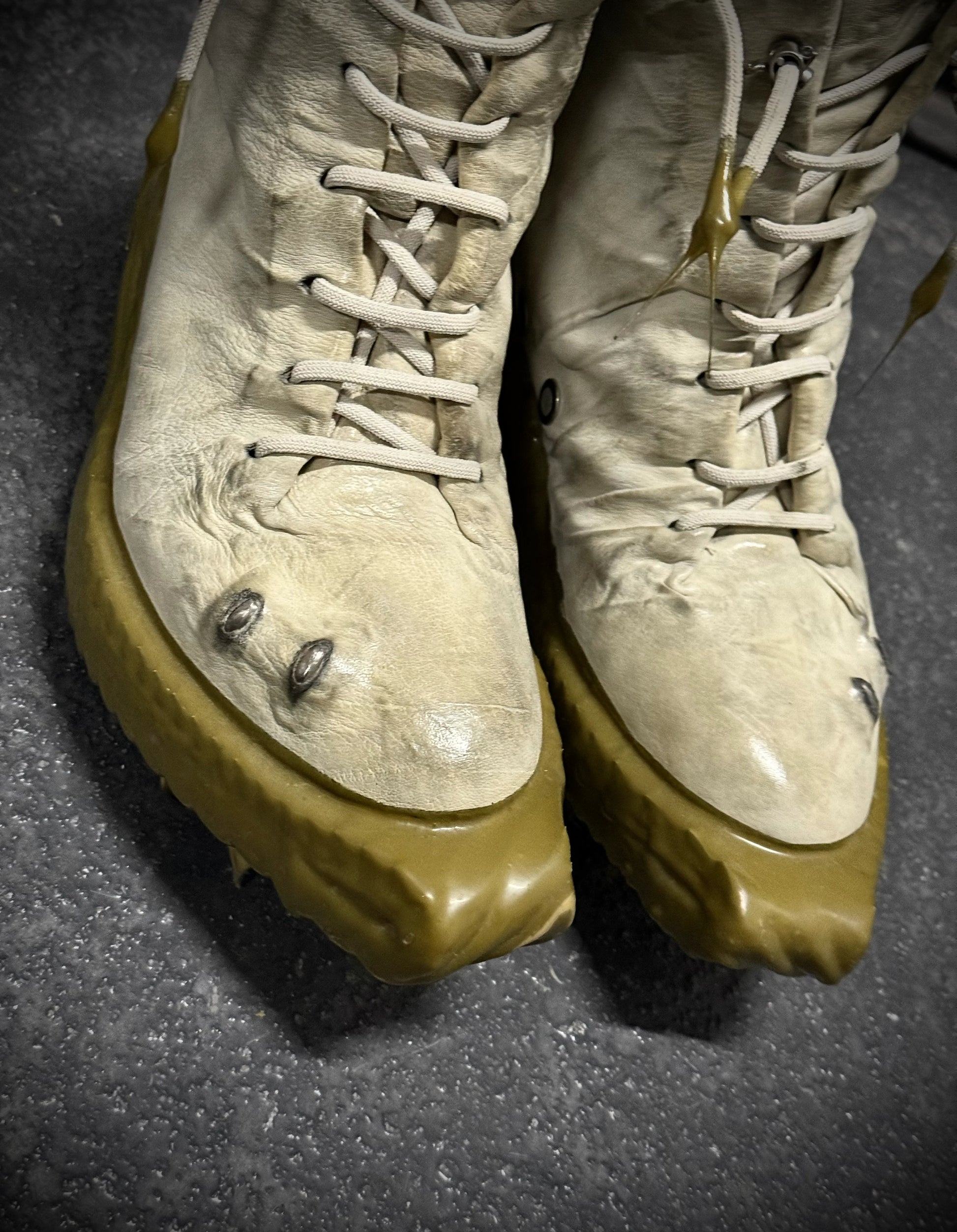 Pair of worn boots with beige soles on a dark surface