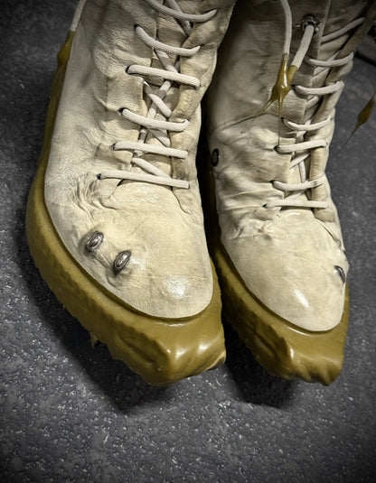Pair of worn boots with beige soles on a dark surface