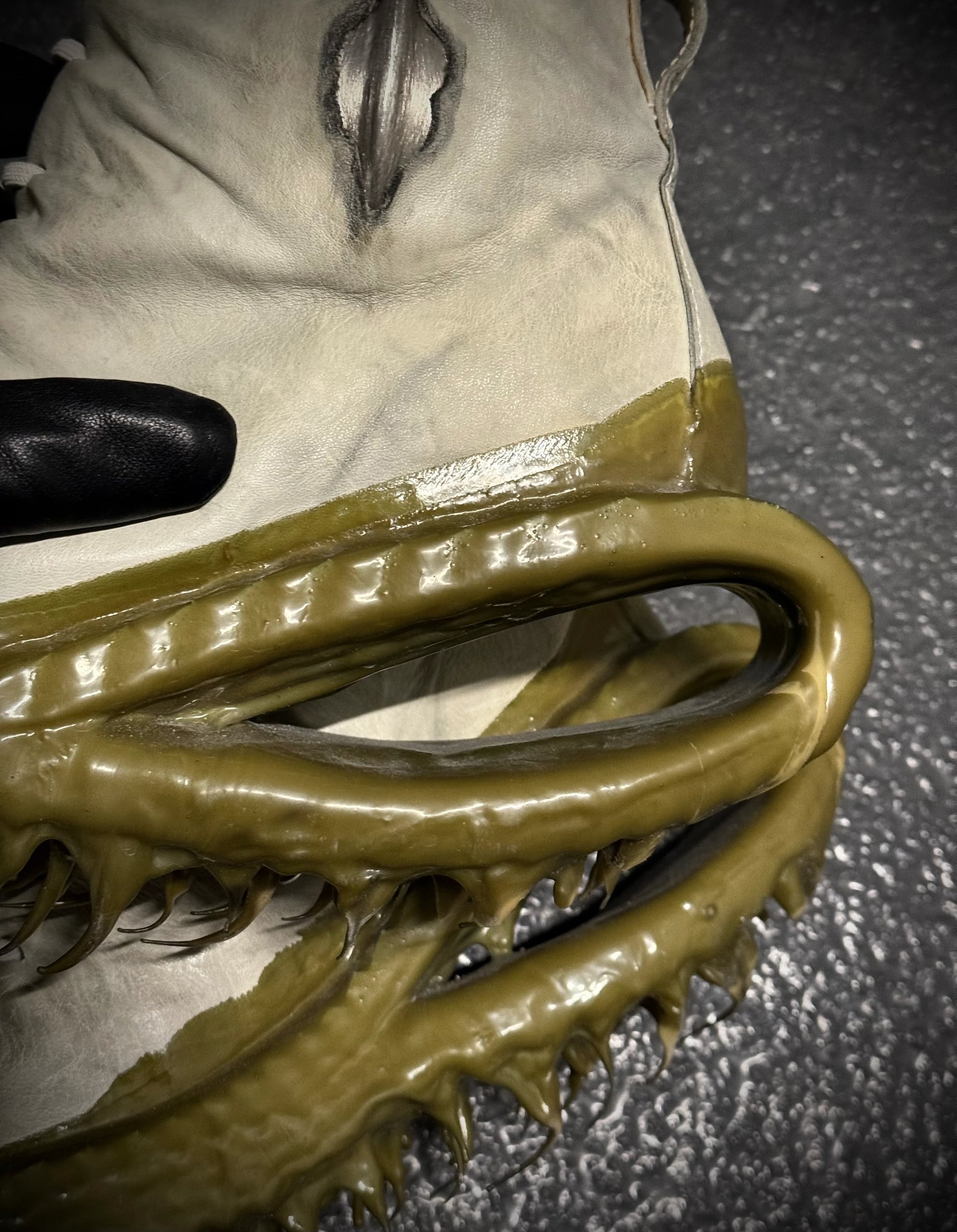 Close-up of a white boot with greenish-brown sole on a dark surface