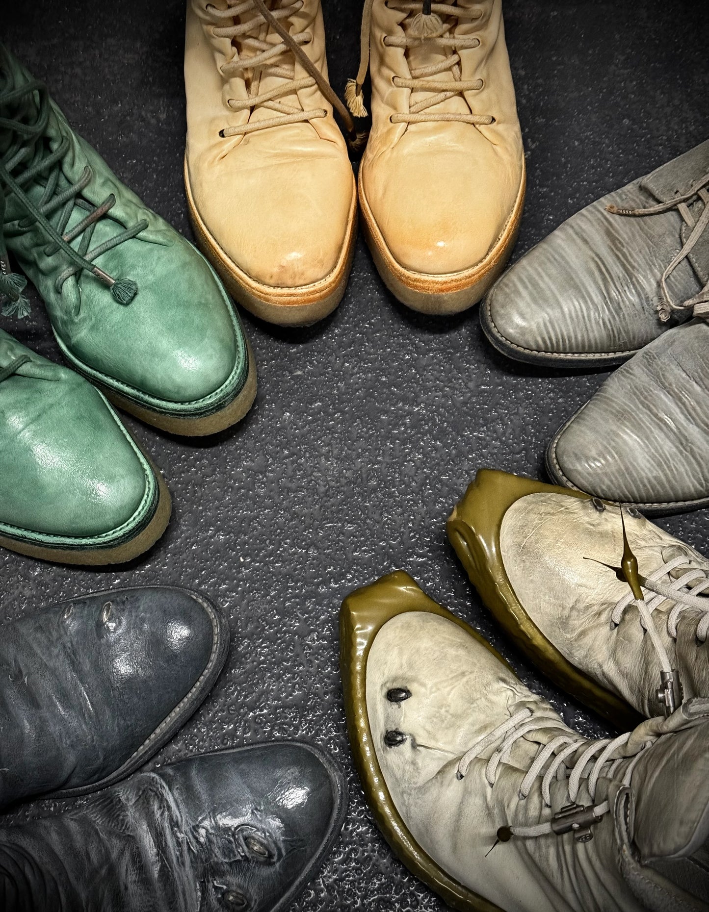 Collection of various colored boots arranged in a circular pattern on a dark surface.