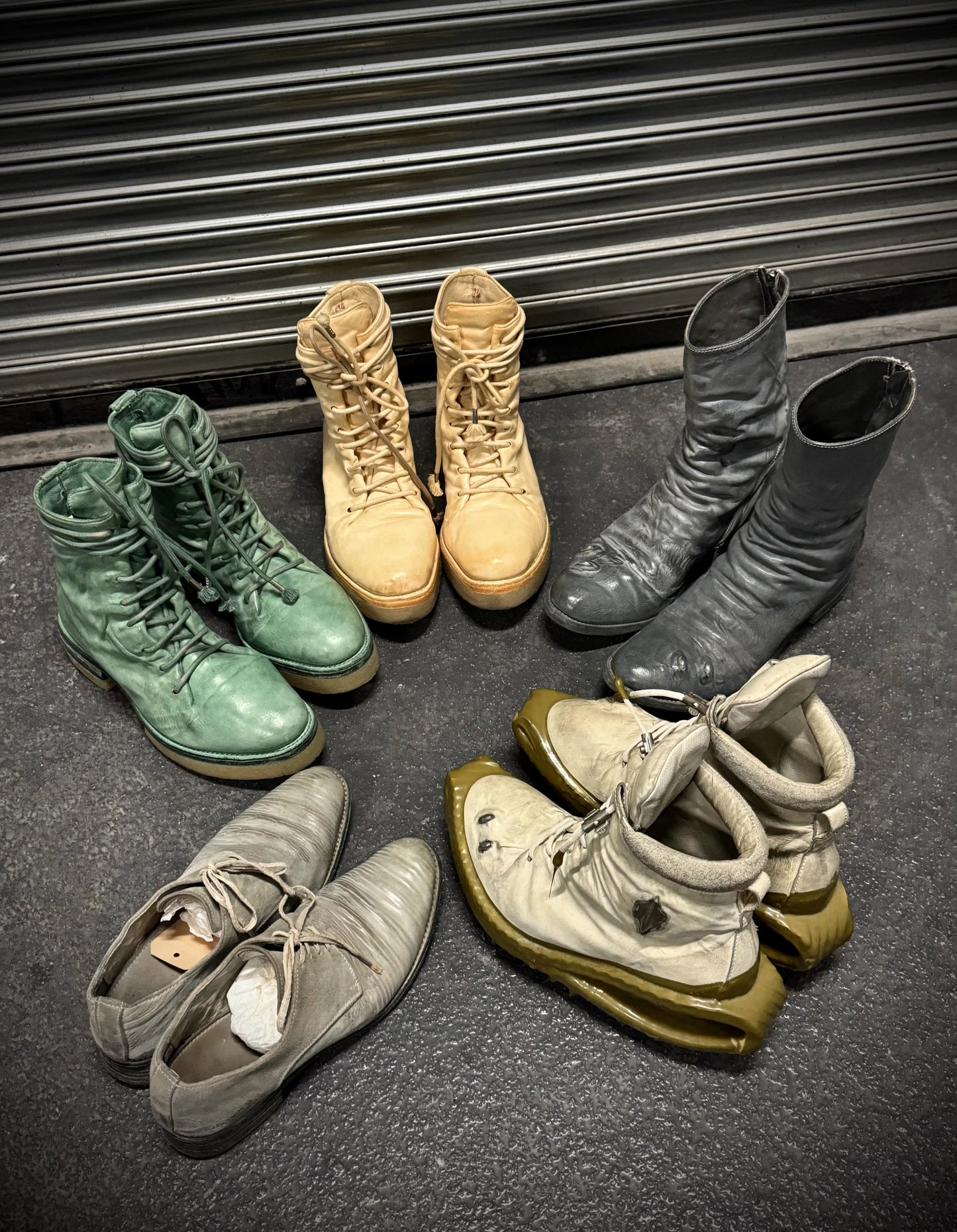 Collection of various boots on a dark surface with a metal shutter in the background
