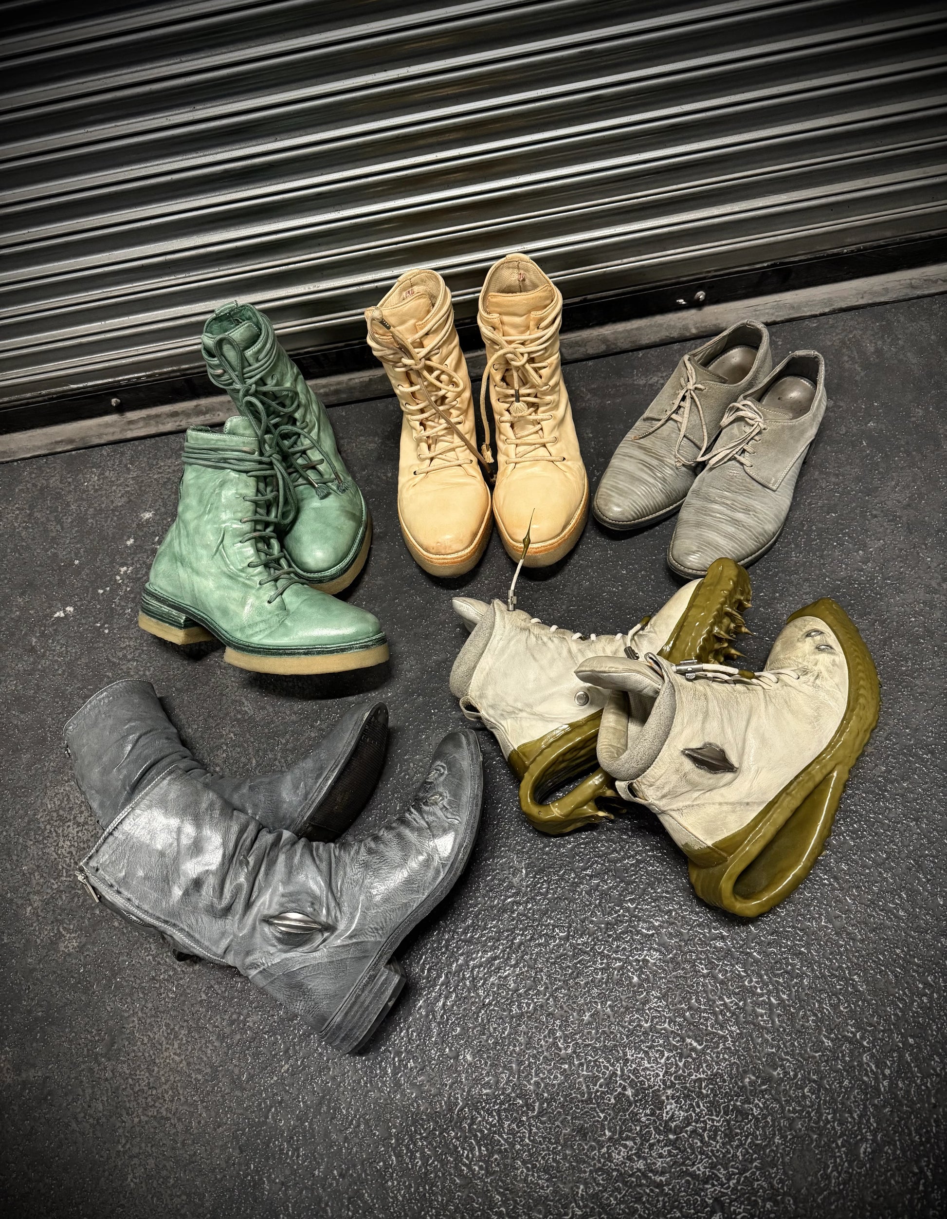 Collection of various boots on a dark surface with a metal shutter in the background