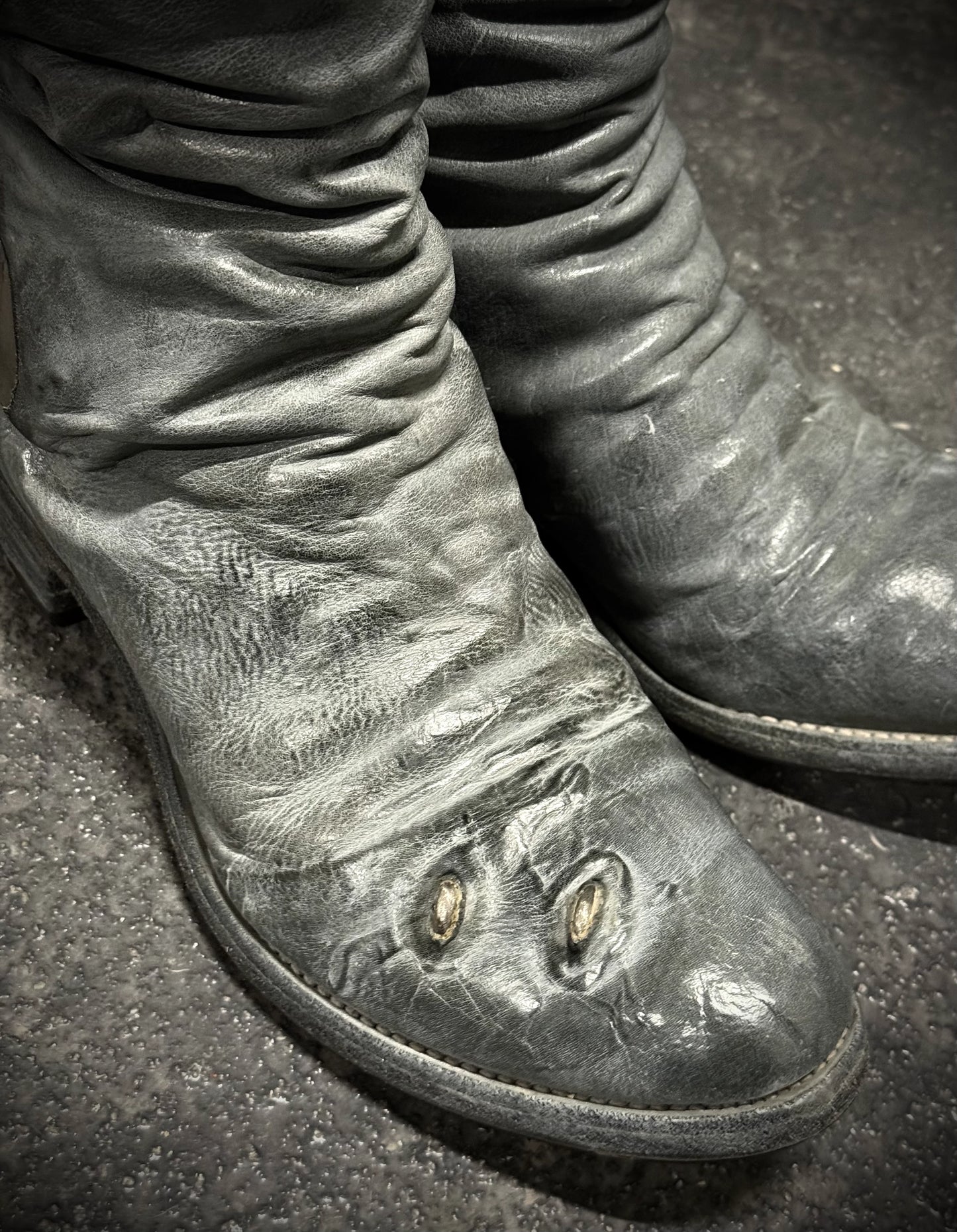 Close-up of worn leather boots on a dark surface