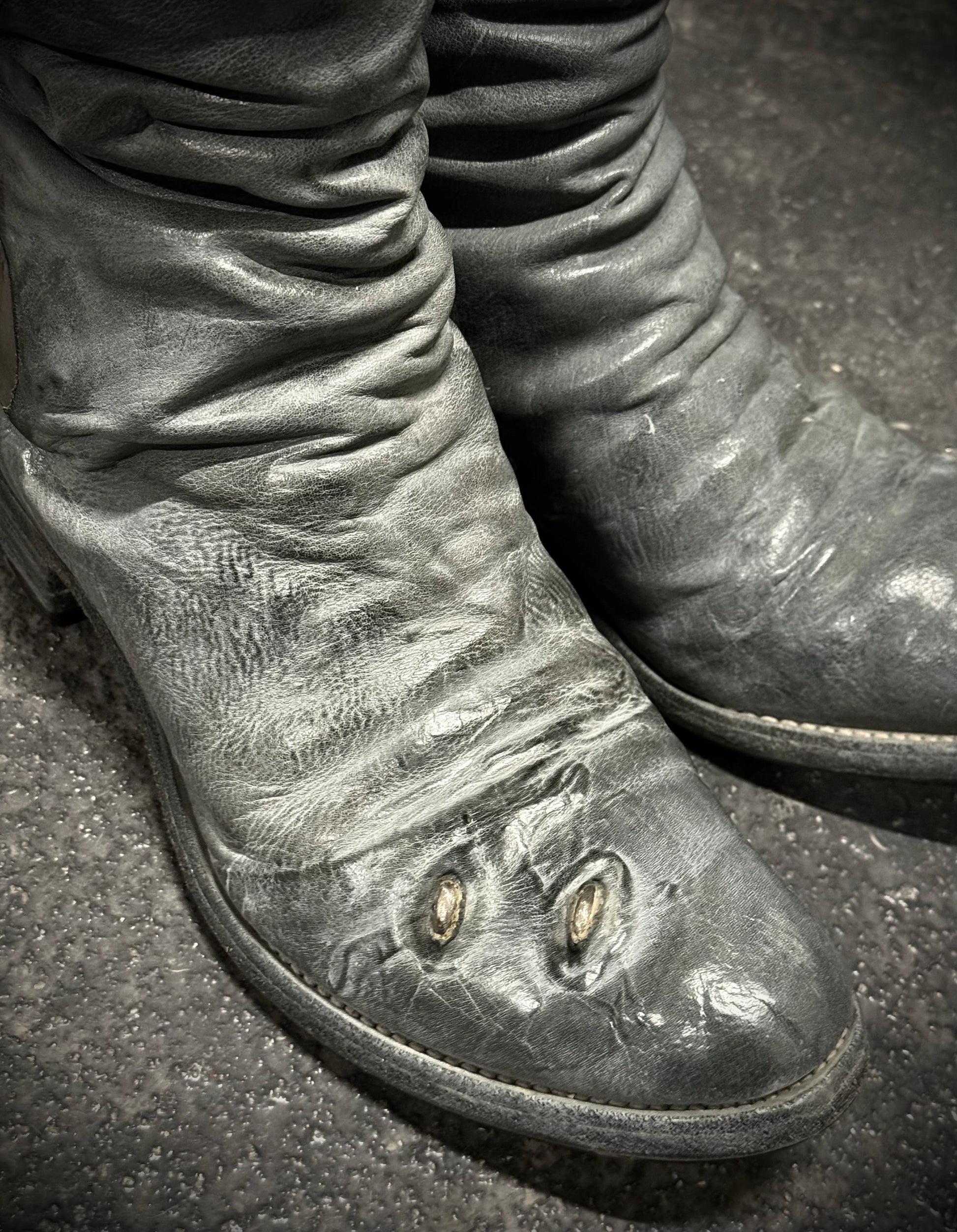 Close-up of worn leather boots on a dark surface