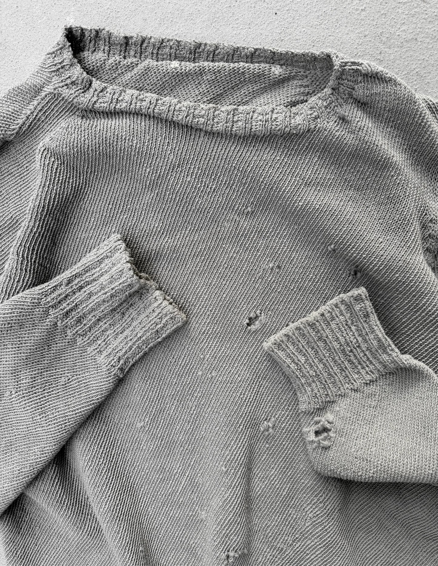 Close-up of a worn gray sweater with visible holes and frayed edges.