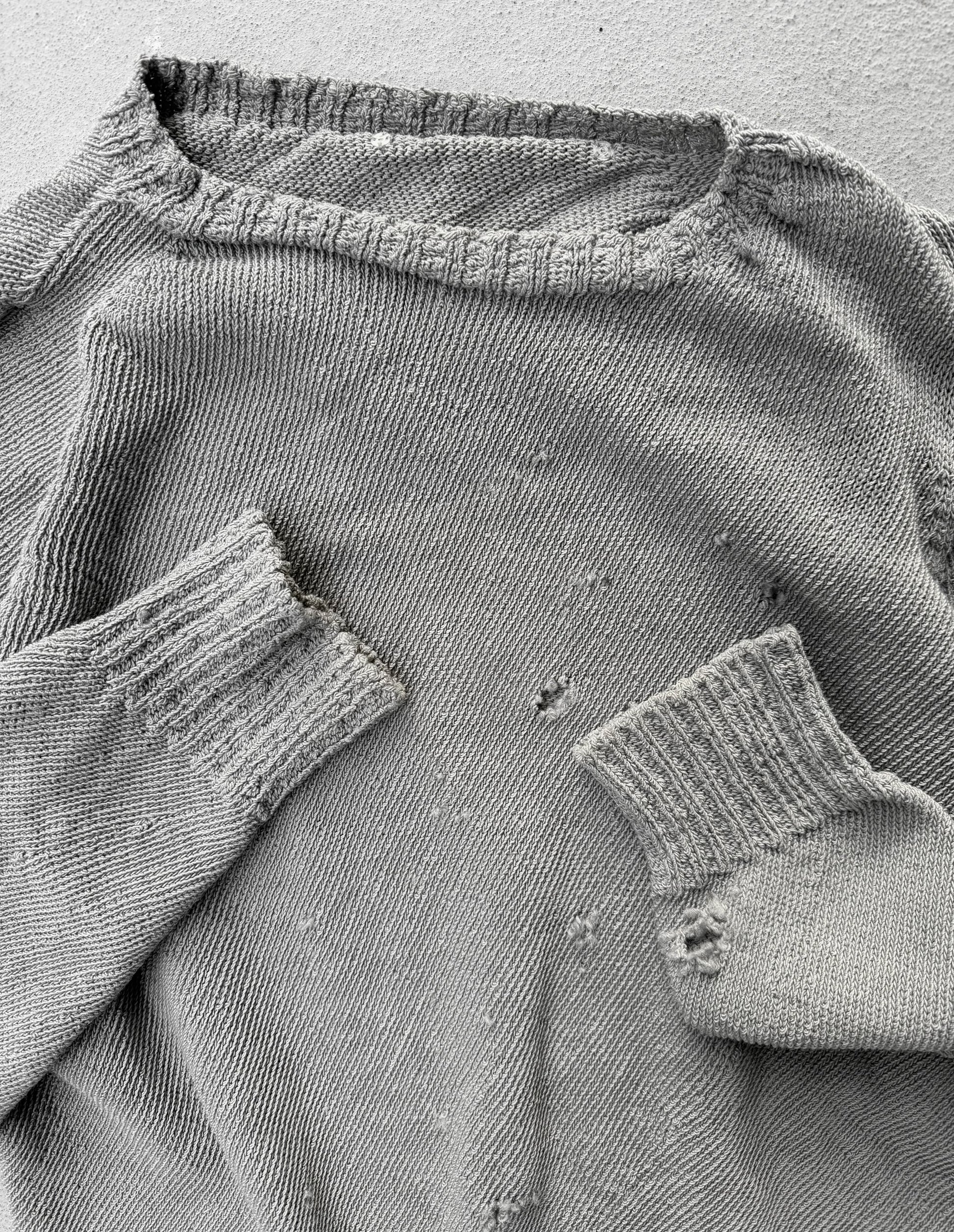 Close-up of a worn gray sweater with visible holes and frayed edges.