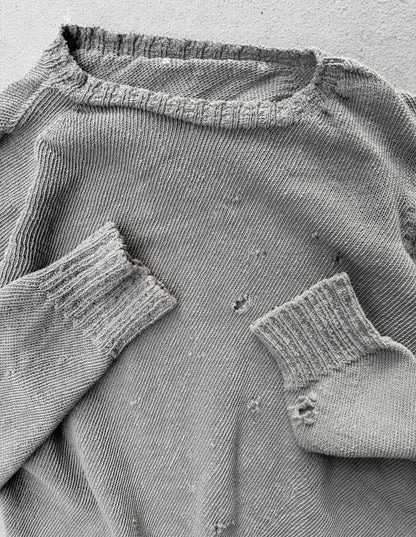 Close-up of a worn gray sweater with visible holes and frayed edges.