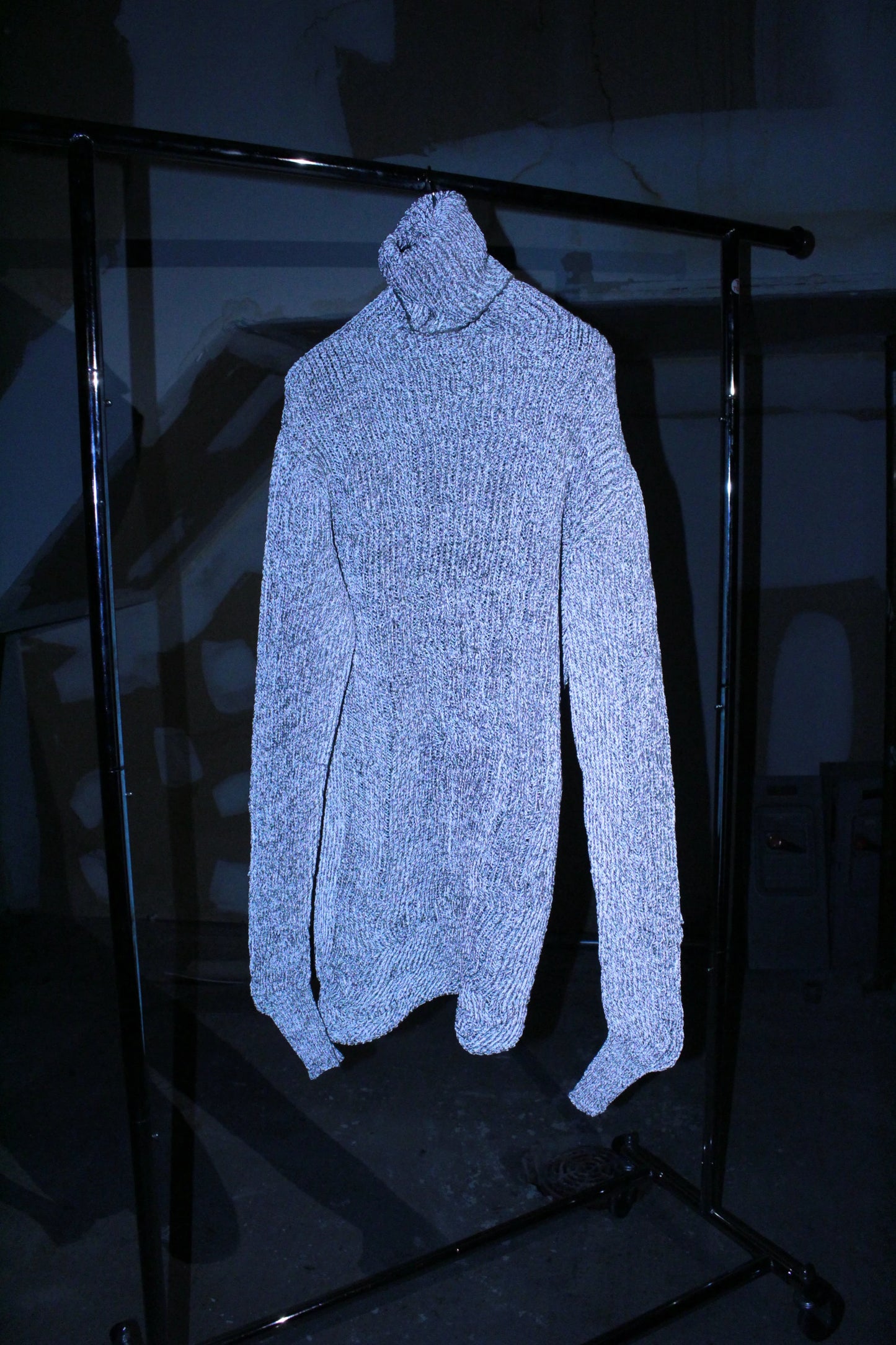 Light blue turtleneck sweater on a black metal stand against a dark background