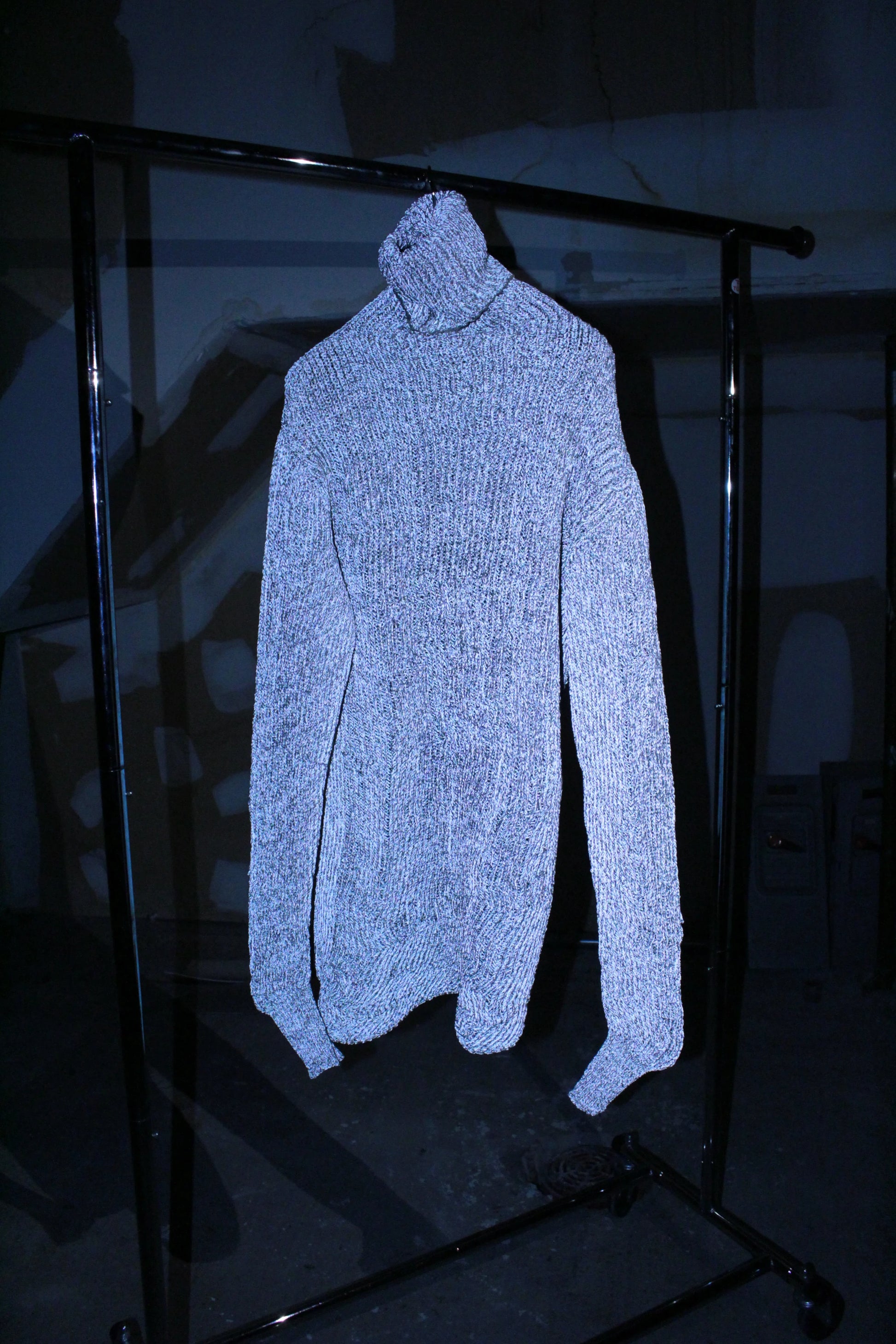 Light blue turtleneck sweater on a black metal stand against a dark background