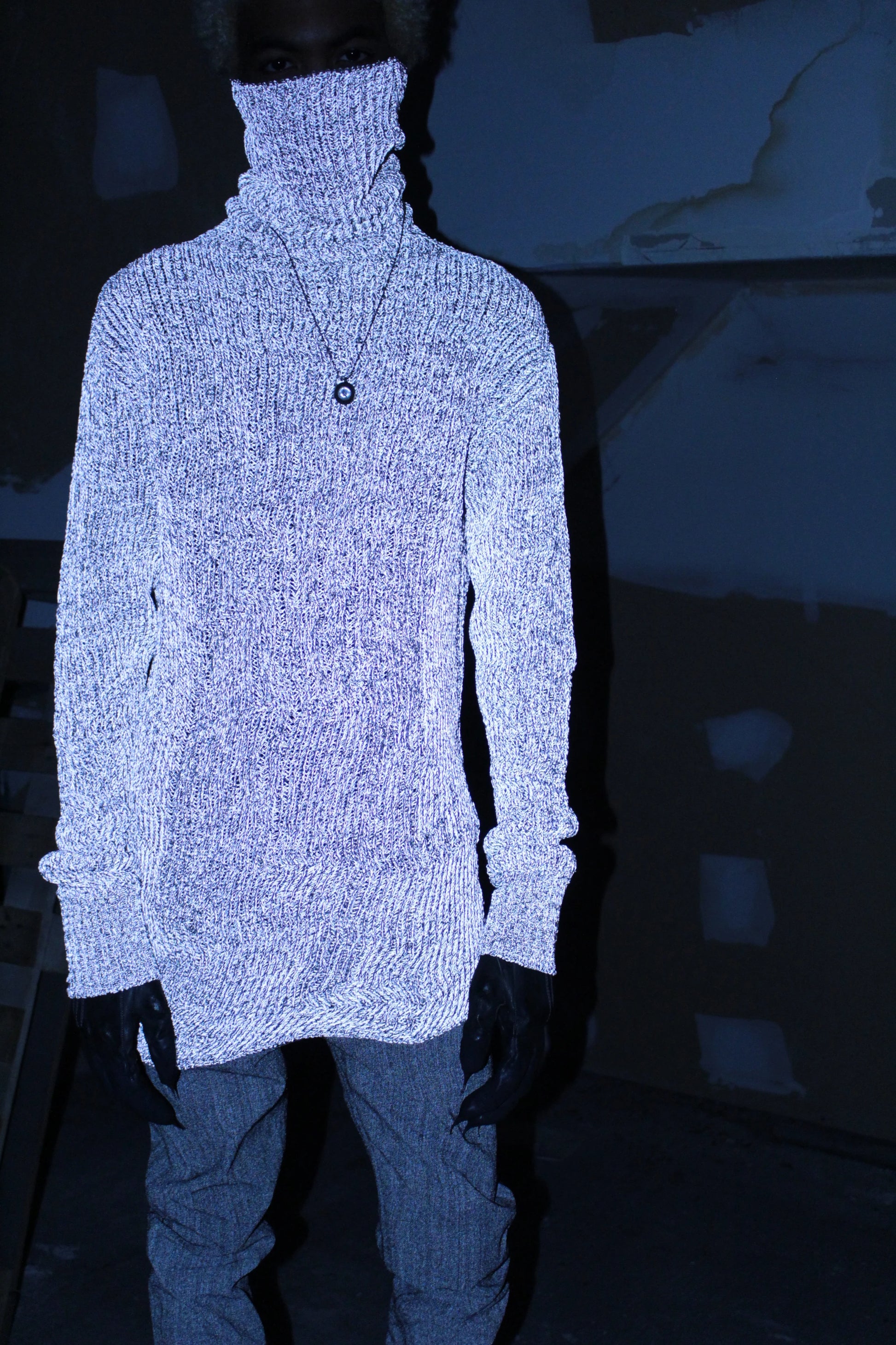 Person wearing a white turtleneck sweater and dark pants in a dark setting