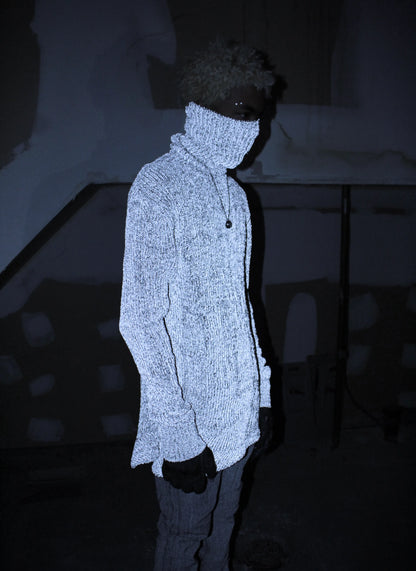 Person wearing a textured white coat and dark hat in a dark setting