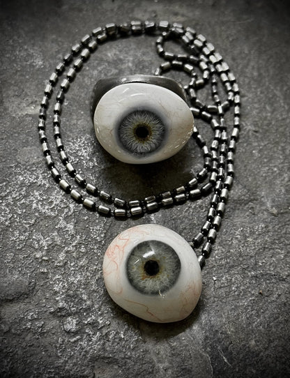 Two eyeball-shaped pendants on a chain against a textured gray background