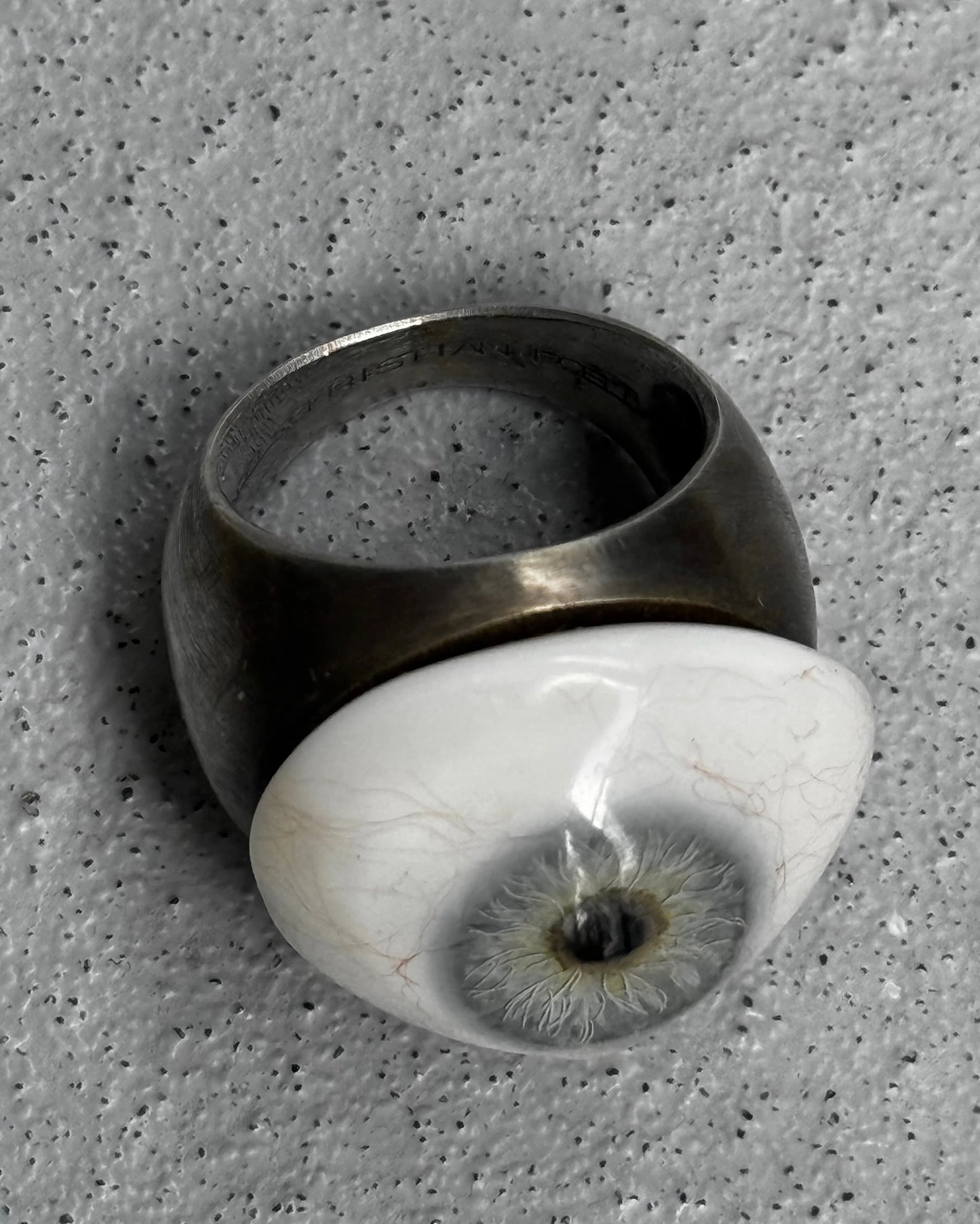 Ring with a unique design featuring a white sphere with an eye-like pattern on a textured gray background