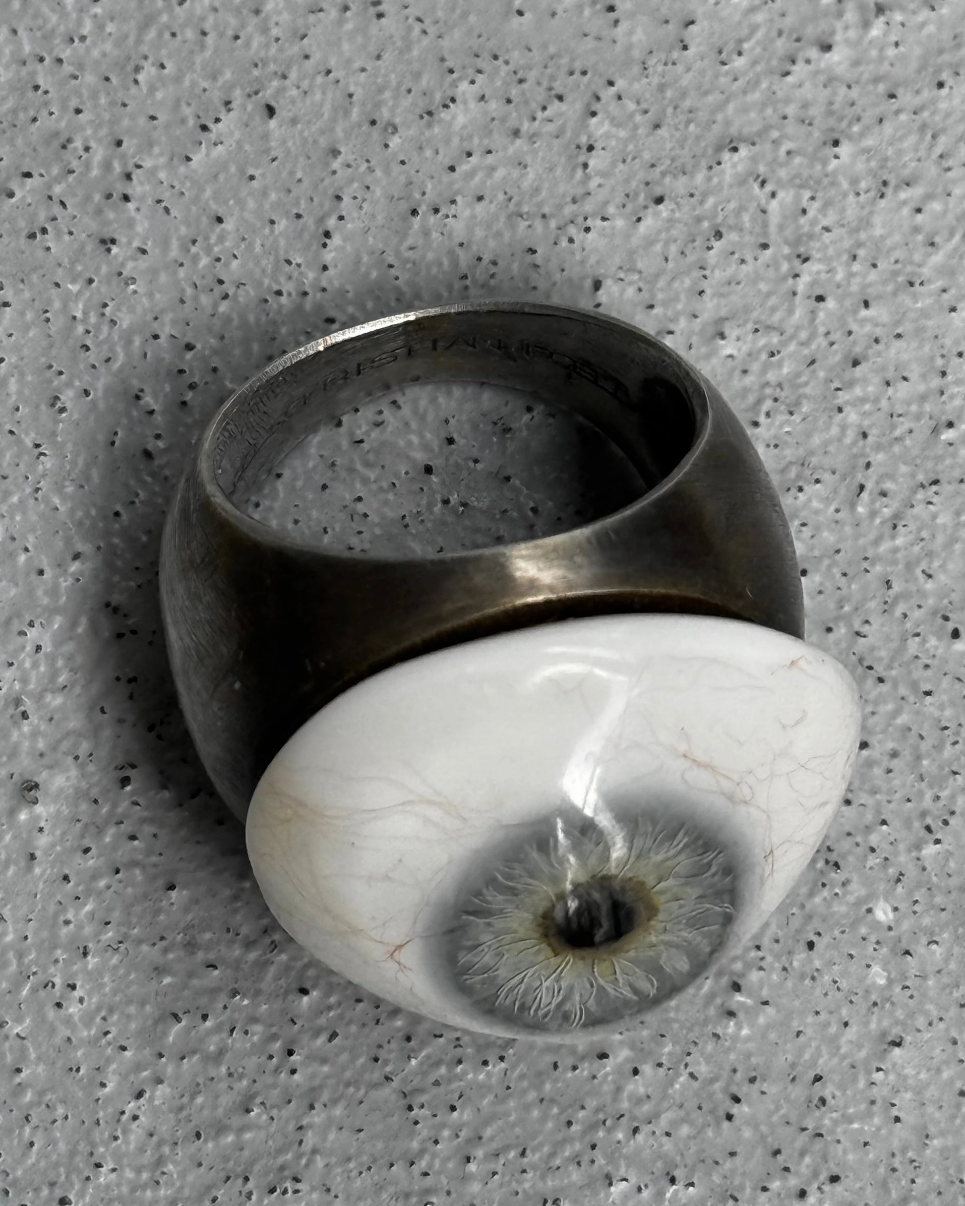Ring with a unique design featuring a white sphere with an eye-like pattern on a textured gray background