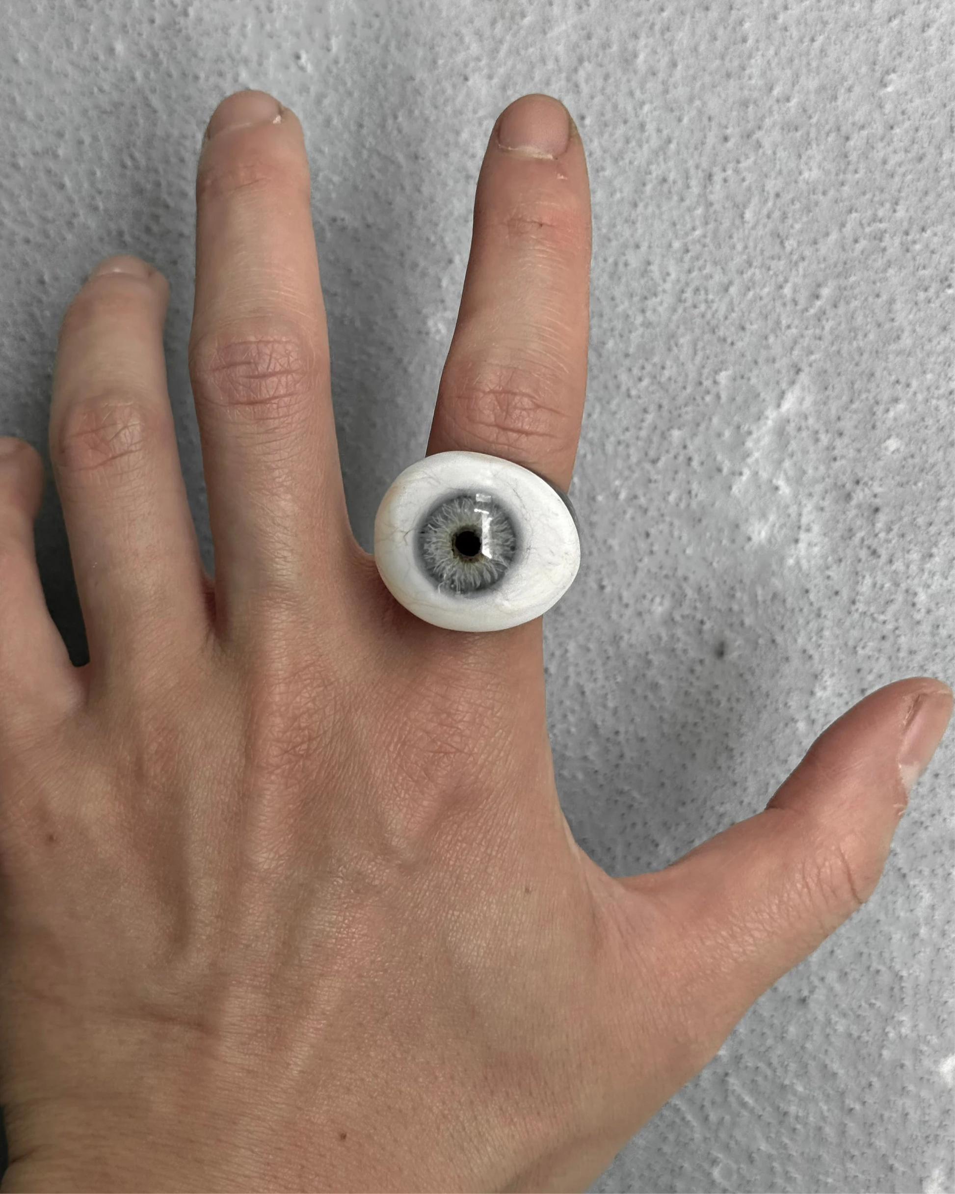 Hand wearing a ring with a white band and black center on a gray background