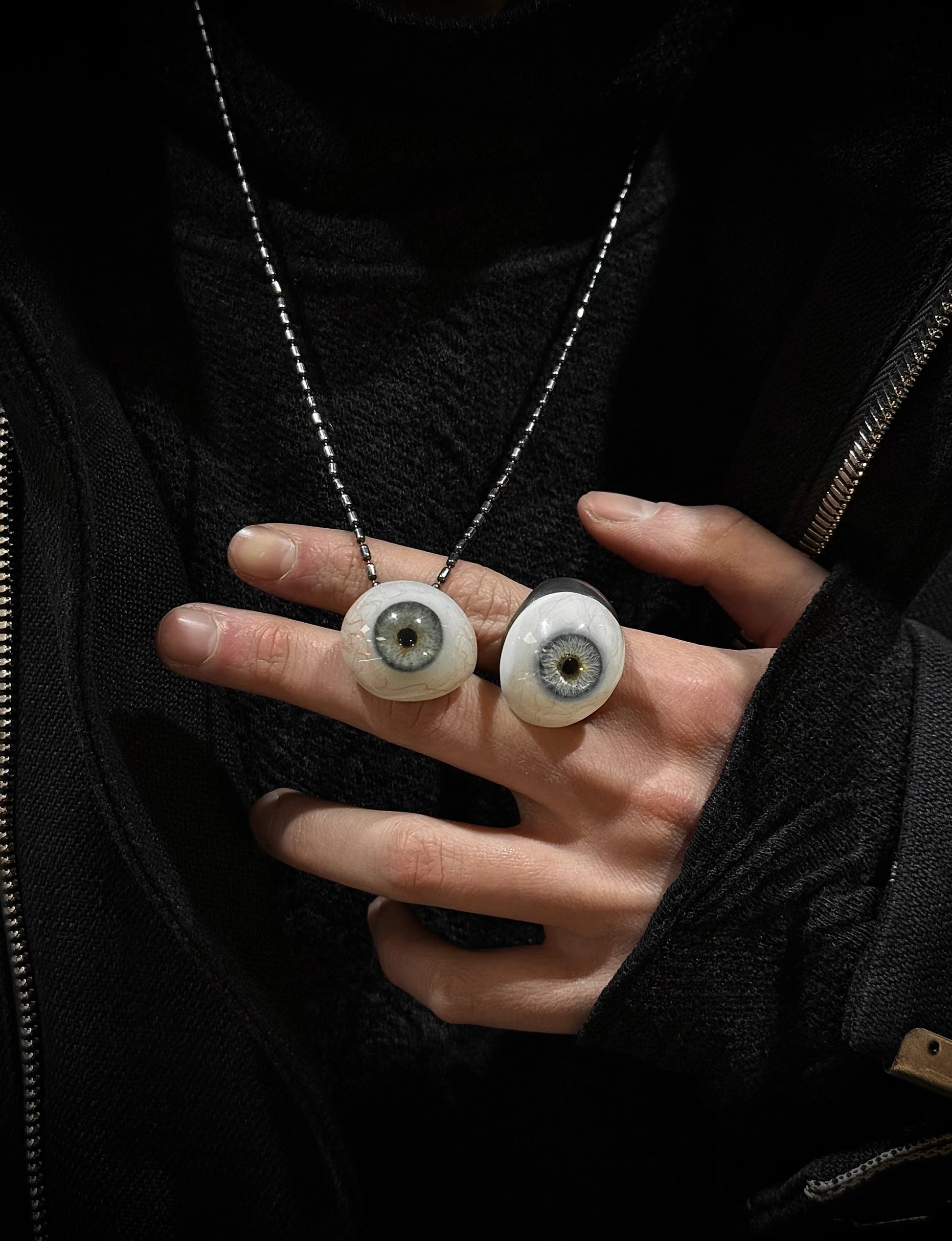 Person holding a necklace with eye-shaped pendants against a dark background