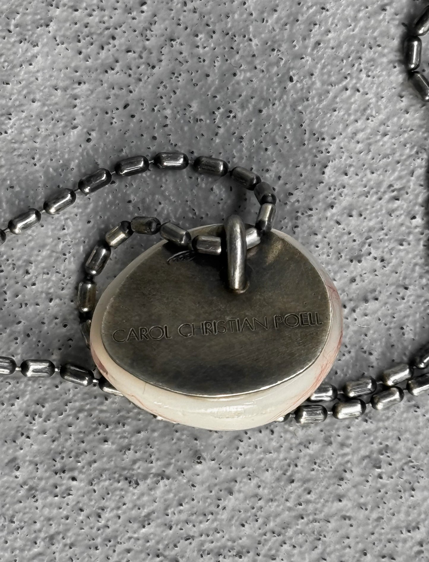 Close-up of a silver necklace with a pendant on a textured gray surface