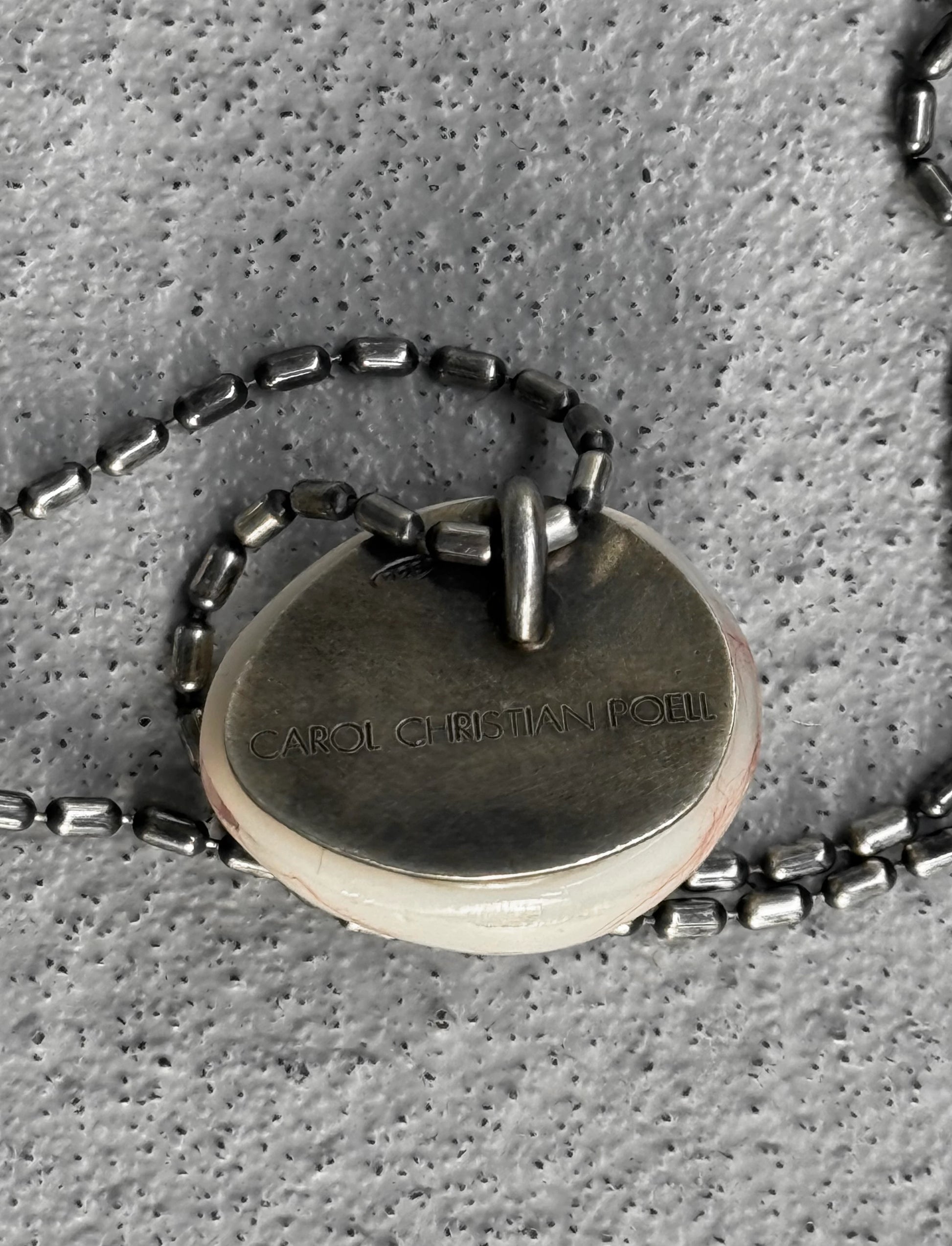 Close-up of a silver necklace with a pendant on a textured gray surface