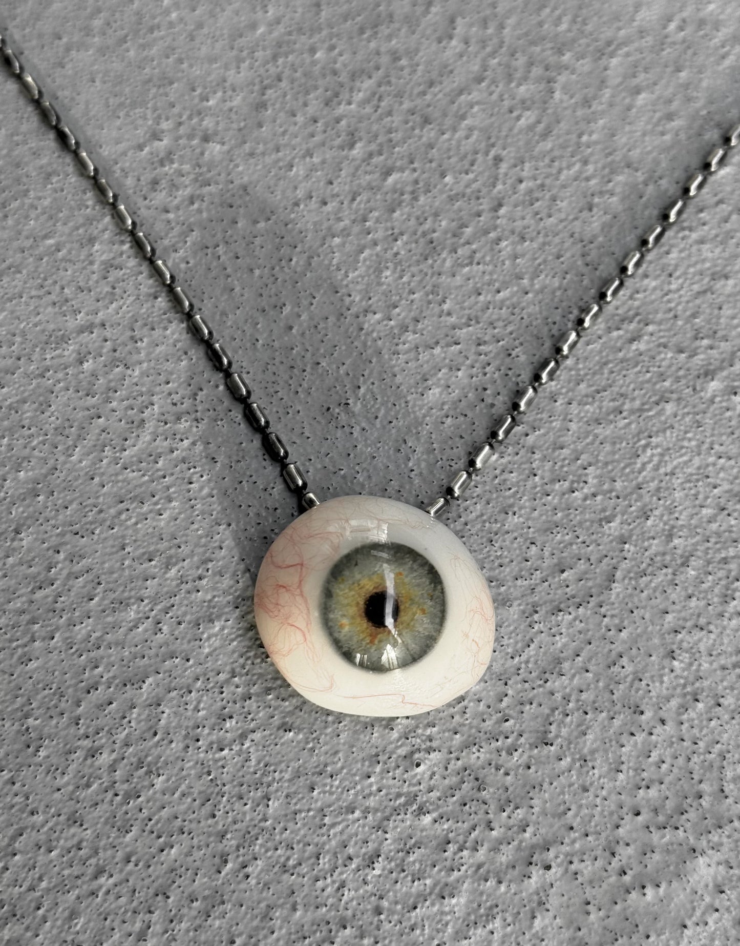 Necklace with a pendant shaped like an eye on a gray textured background