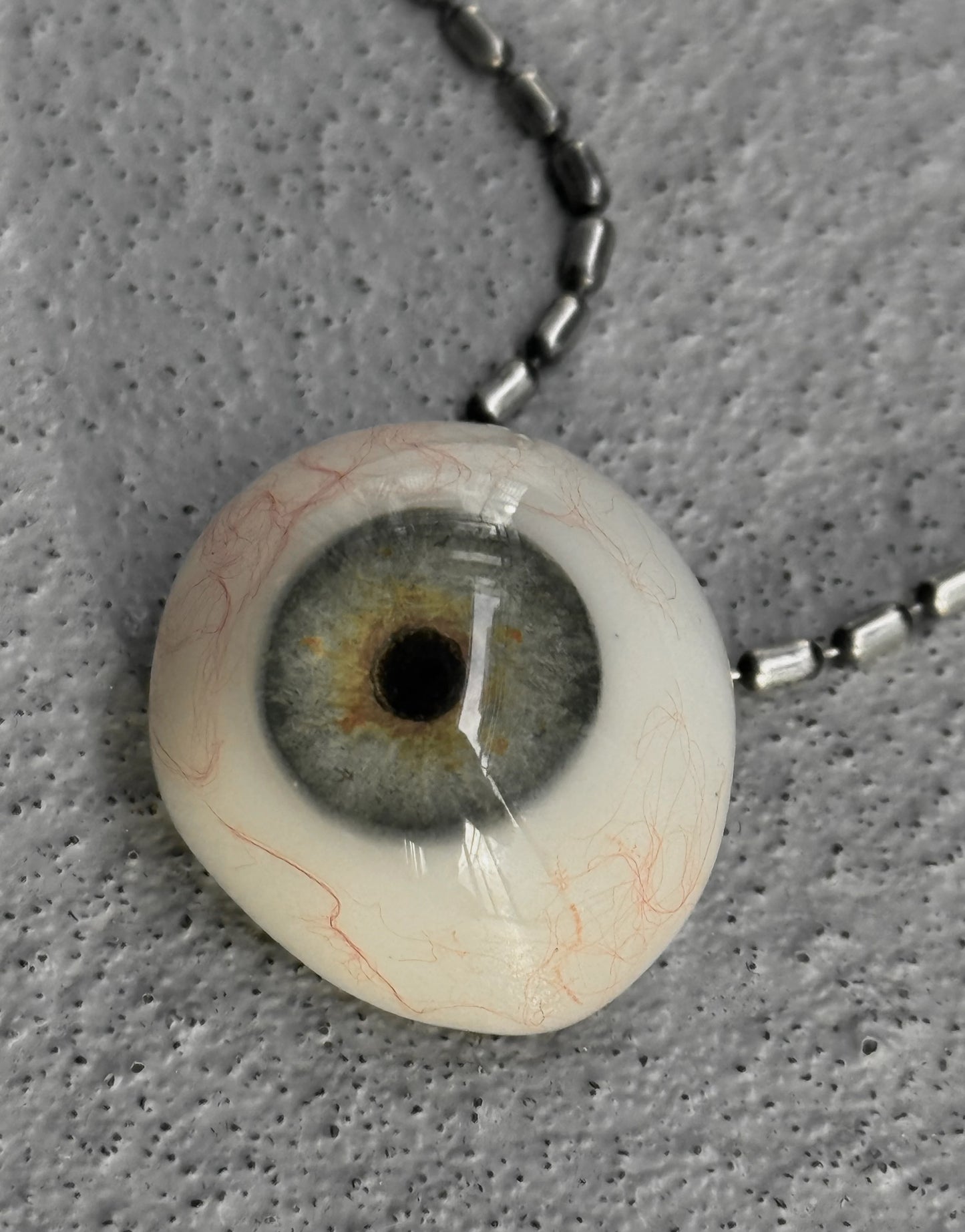 Artificial eye on a chain against a gray background