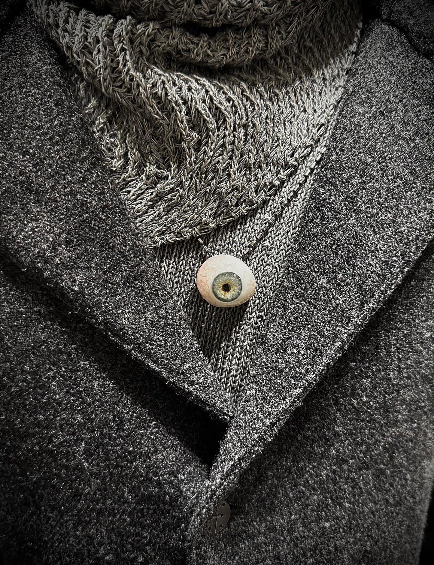 Close-up of a textured scarf and coat with a button, in grayscale.