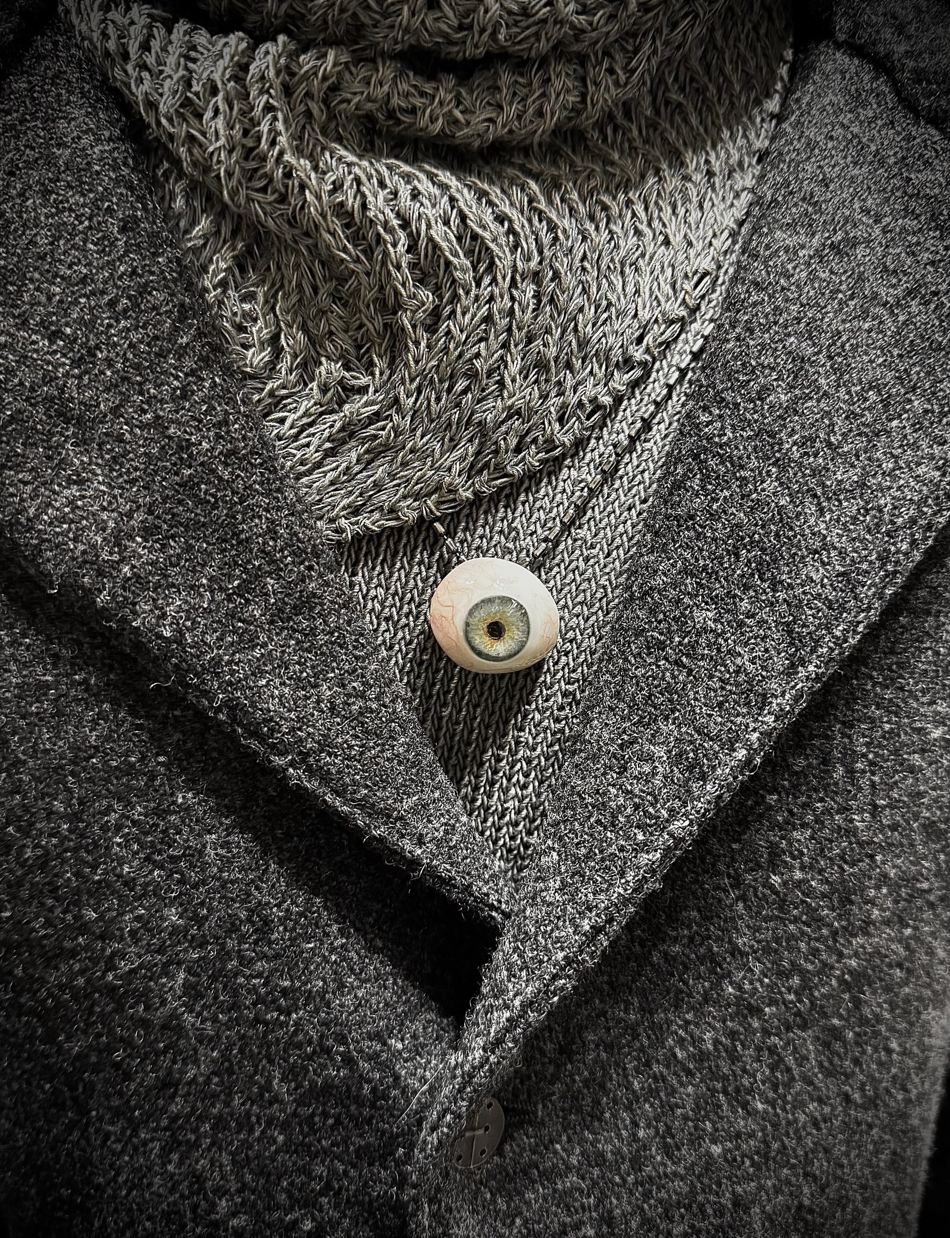Close-up of a textured scarf and coat with a button, in grayscale.