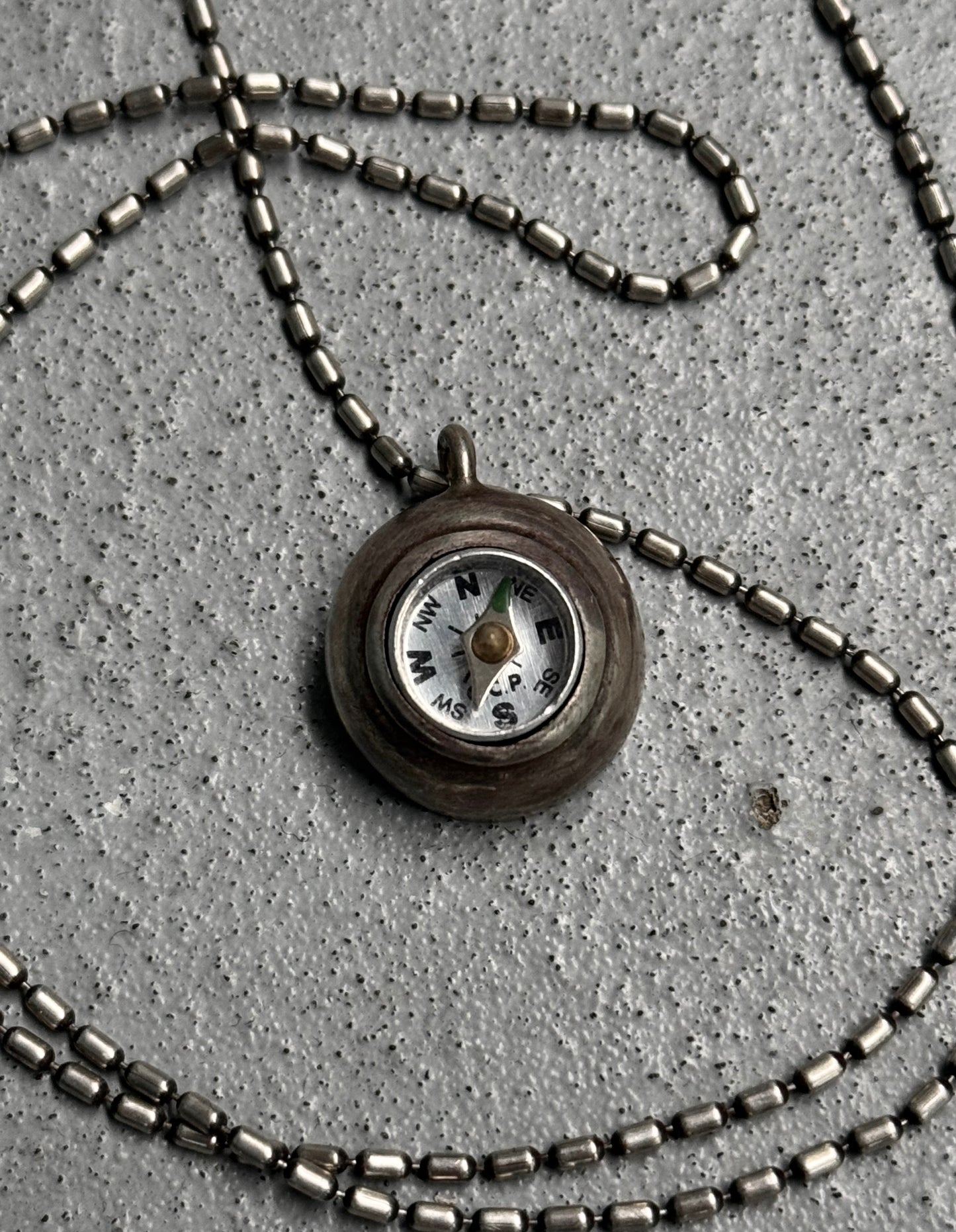 Necklace with a compass pendant on a concrete surface