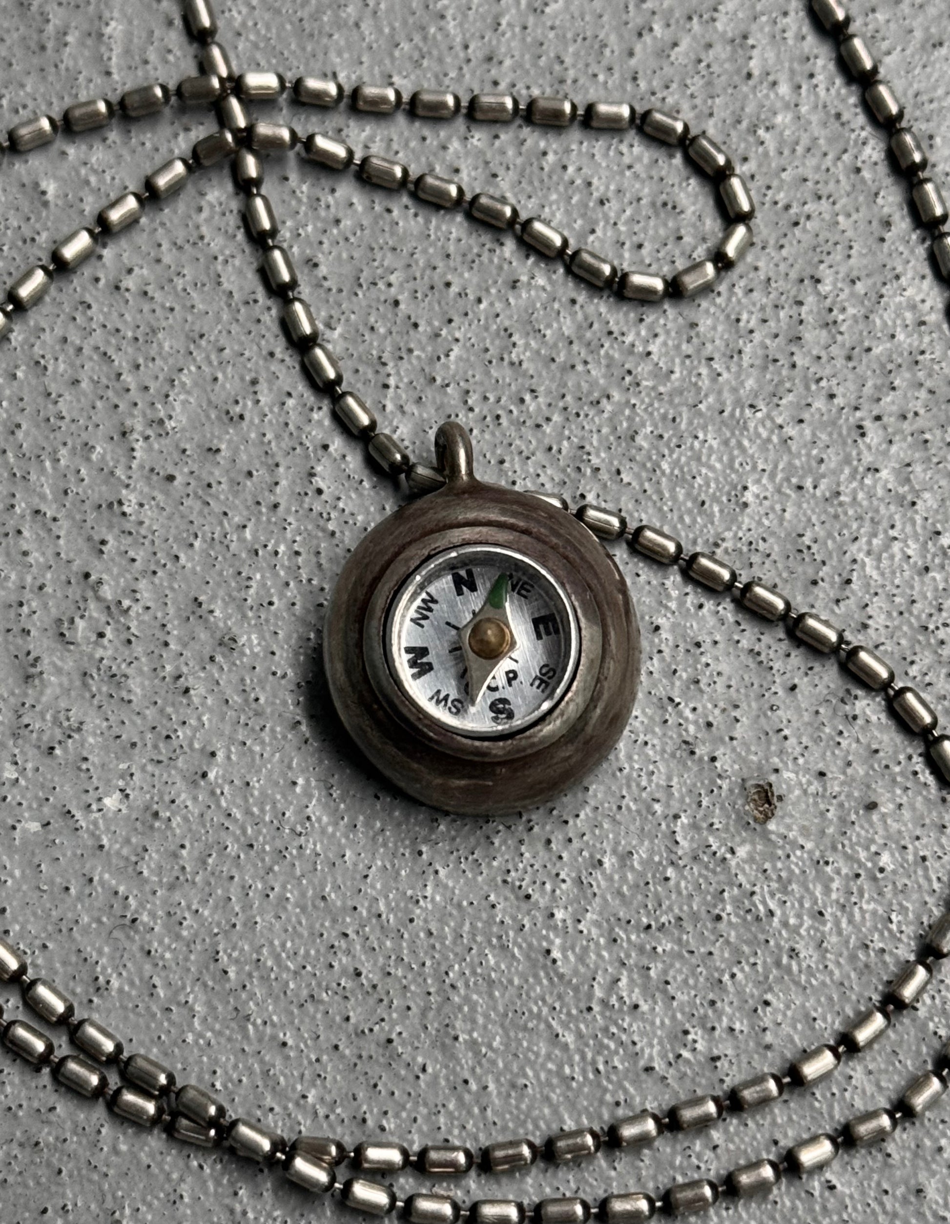 Necklace with a compass pendant on a concrete surface