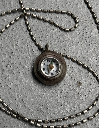 Necklace with a compass pendant on a concrete surface