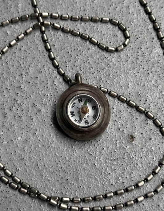Necklace with a compass pendant on a concrete surface