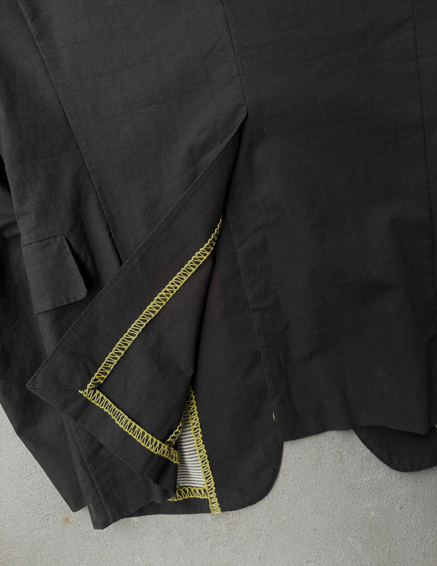 Close-up of a black garment with yellow stitching on a gray surface