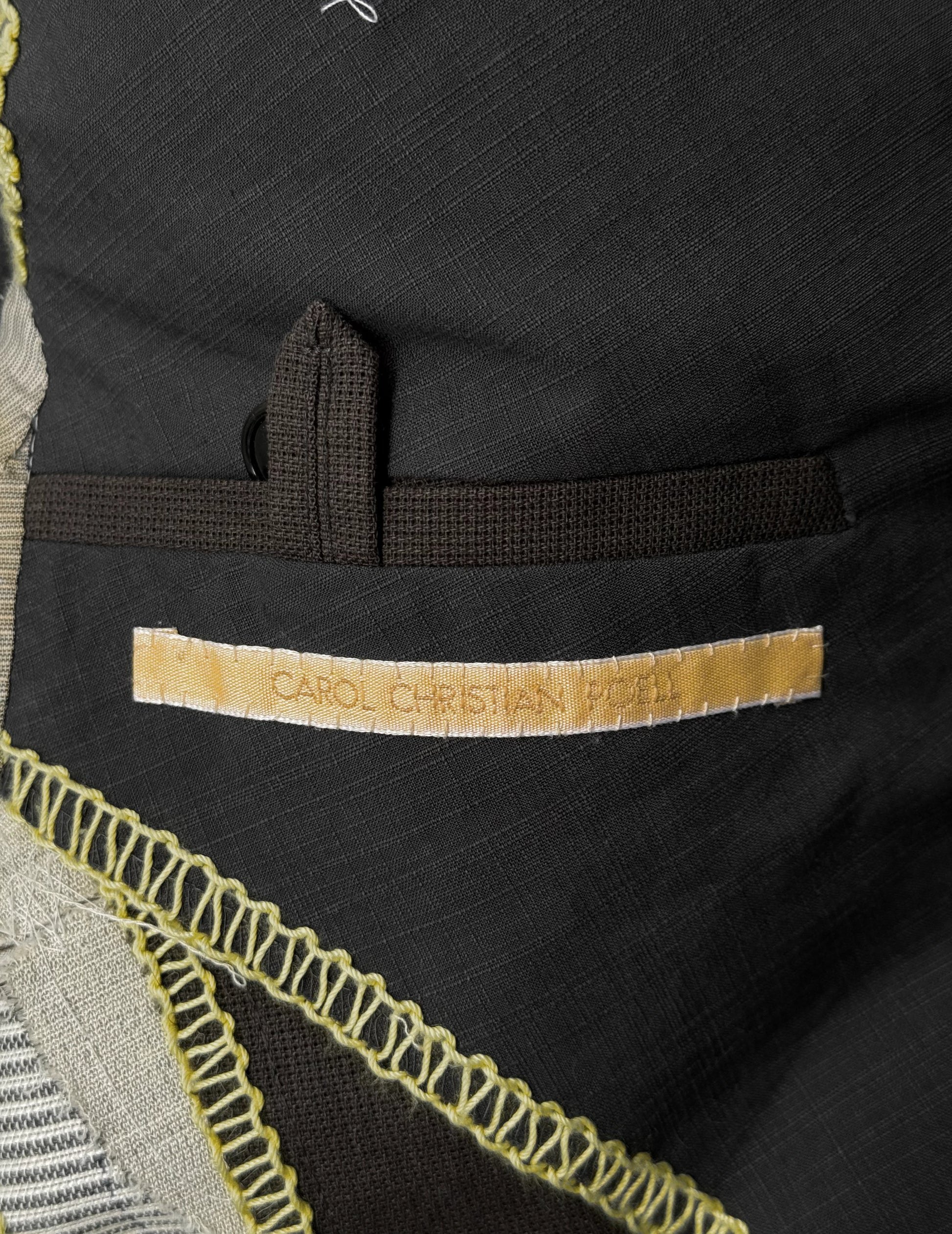 Close-up of a black garment with 'Carol Christian Poell' label, featuring intricate yellow stitching.