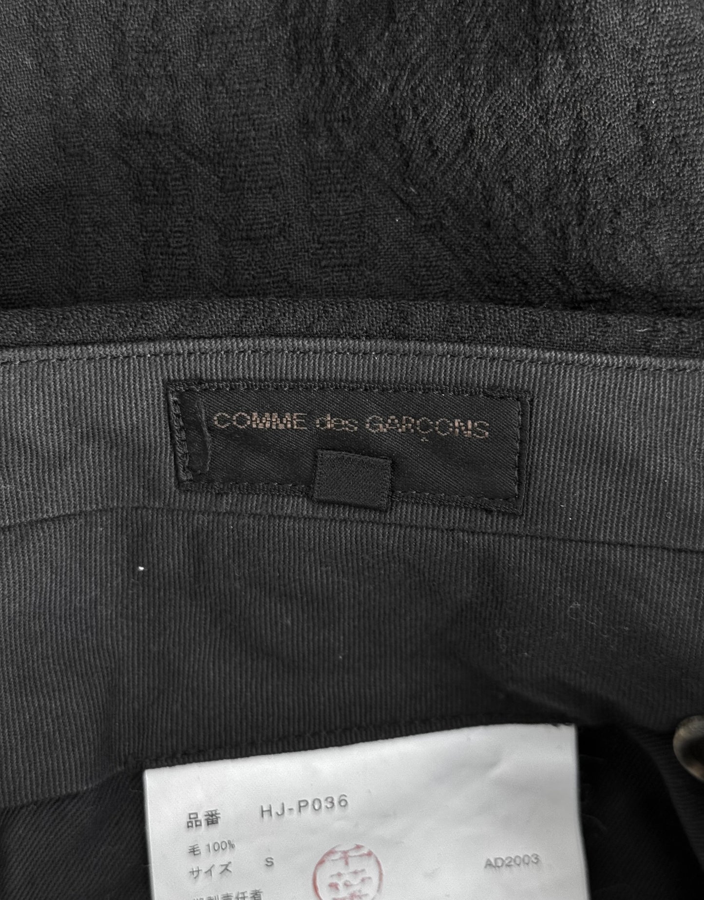 Black fabric with 'Comme des Garcons' label and a tag at the bottom.