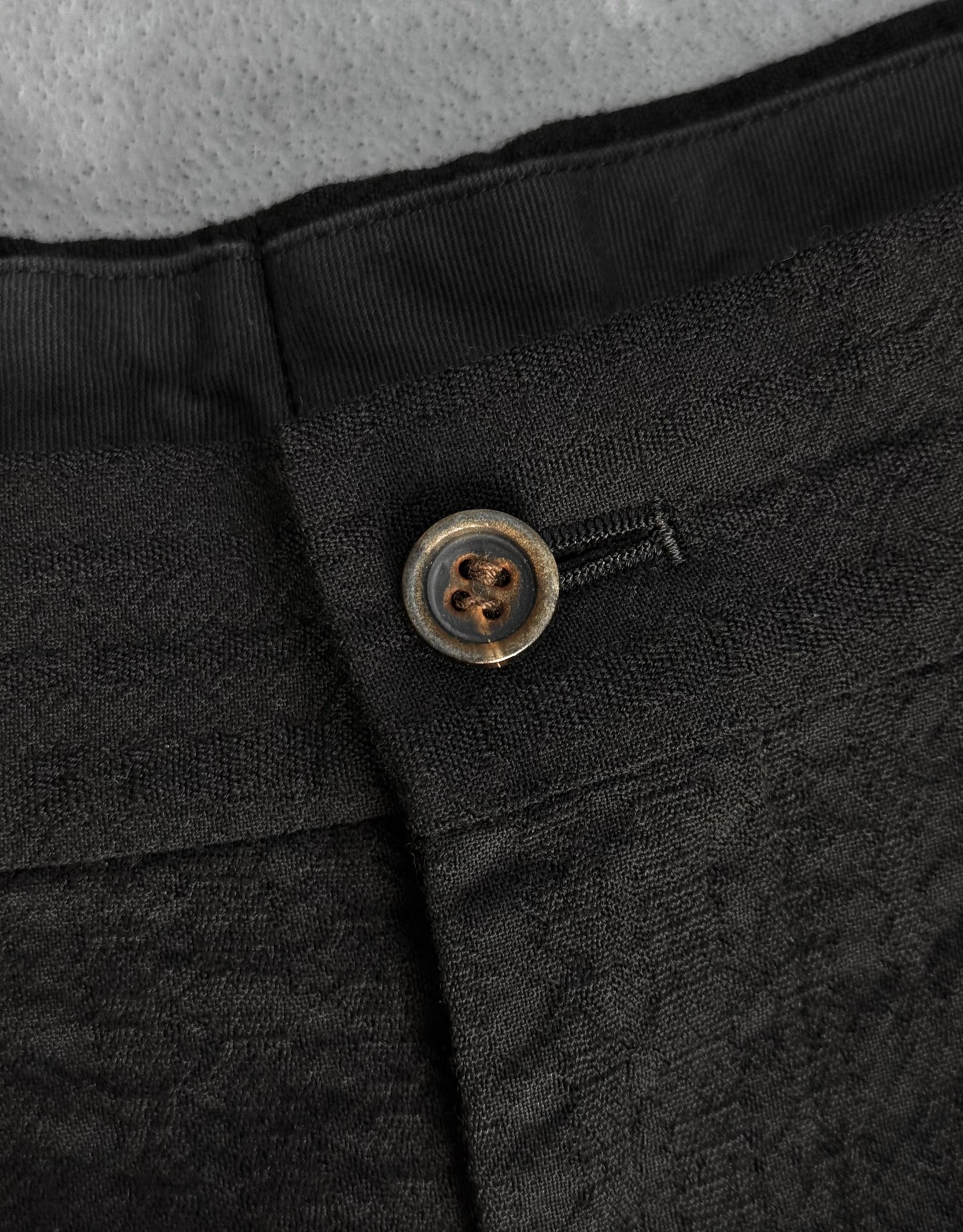 Close-up of a black textured fabric with a button on a gray background