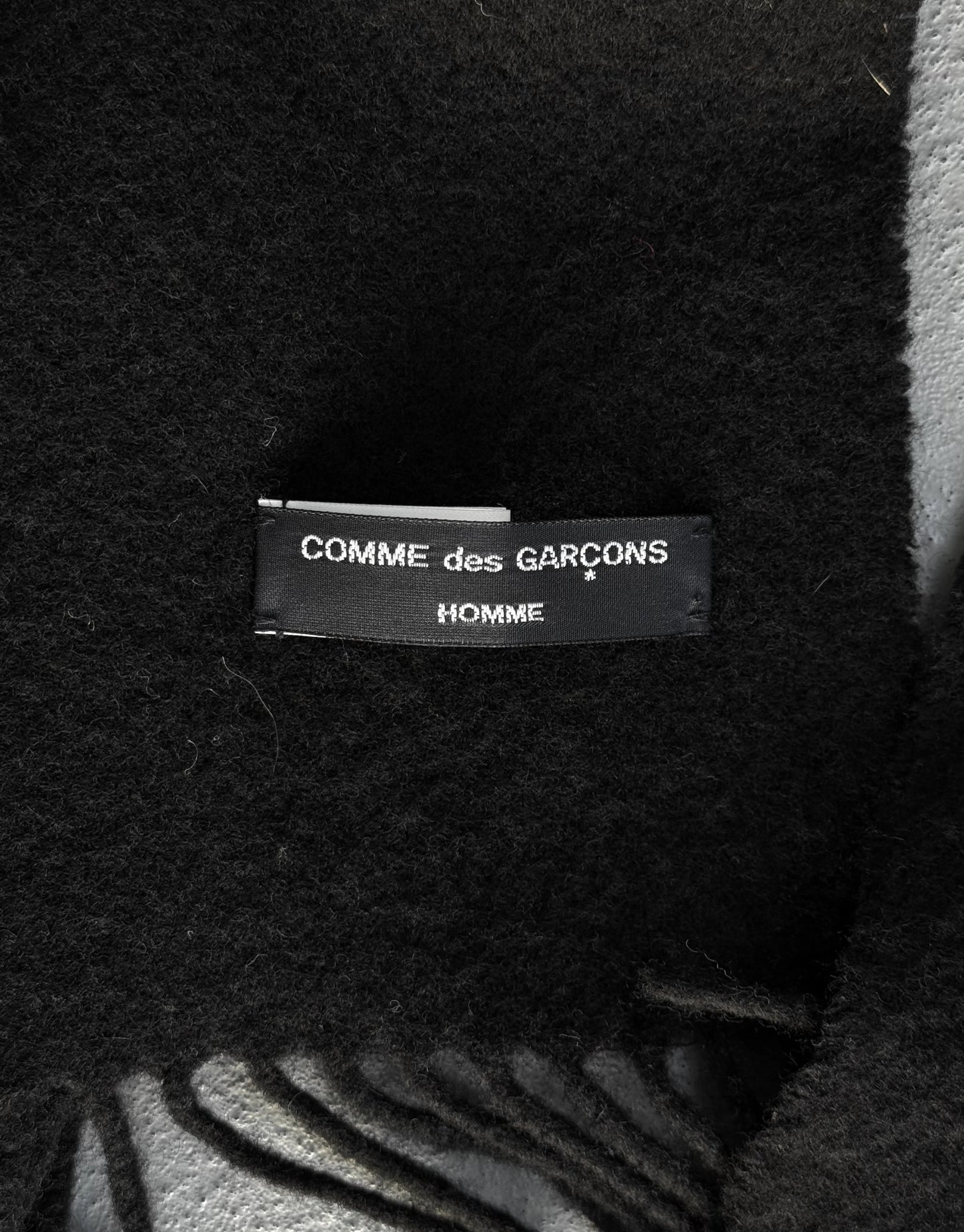 Close-up of a 'COMME des GARCONS HOMME' label on a textured fabric background.