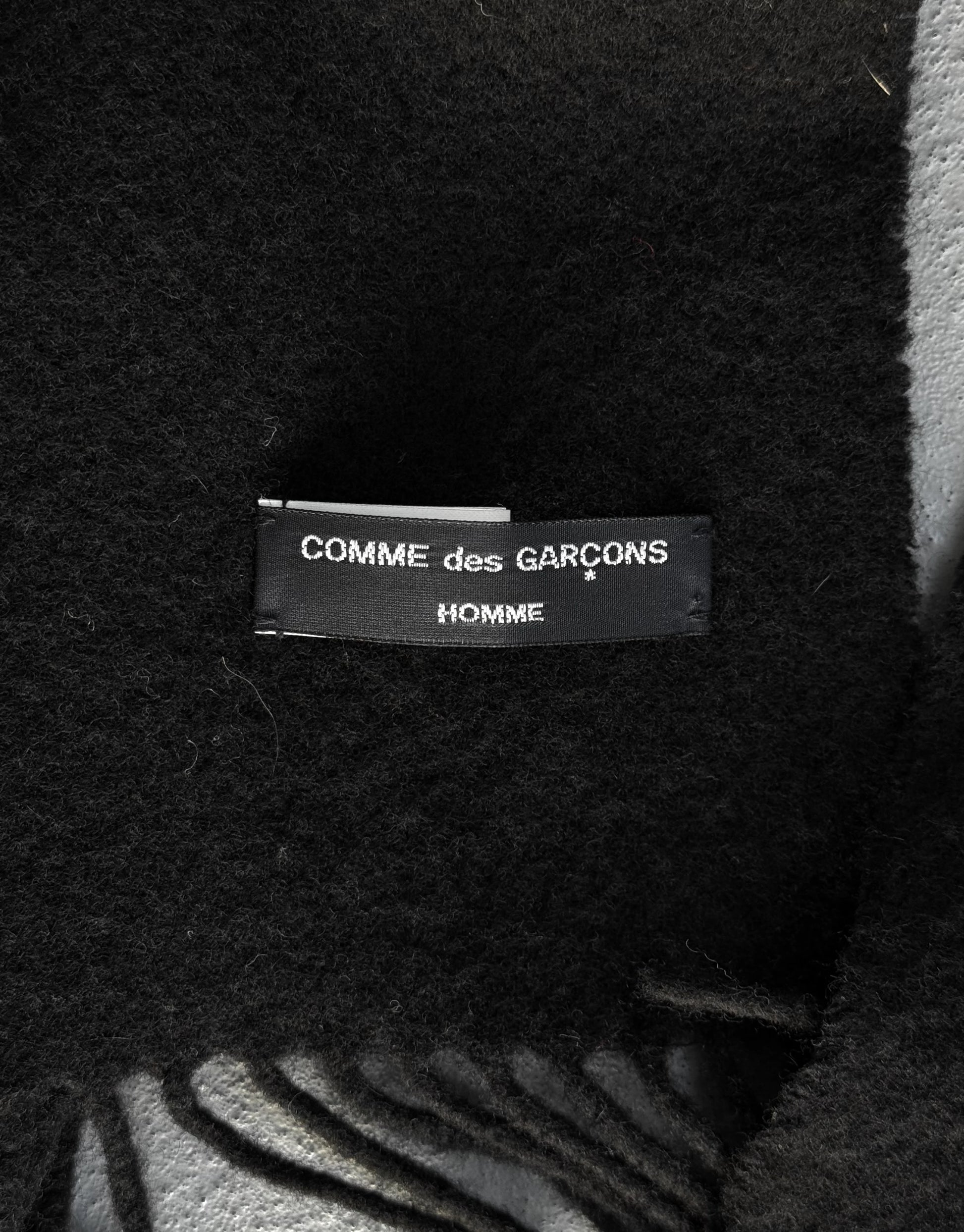 Close-up of a 'COMME des GARCONS HOMME' label on a textured fabric background.