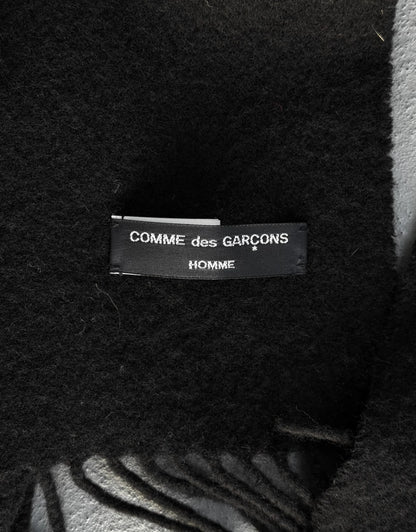 Close-up of a 'COMME des GARCONS HOMME' label on a textured fabric background.