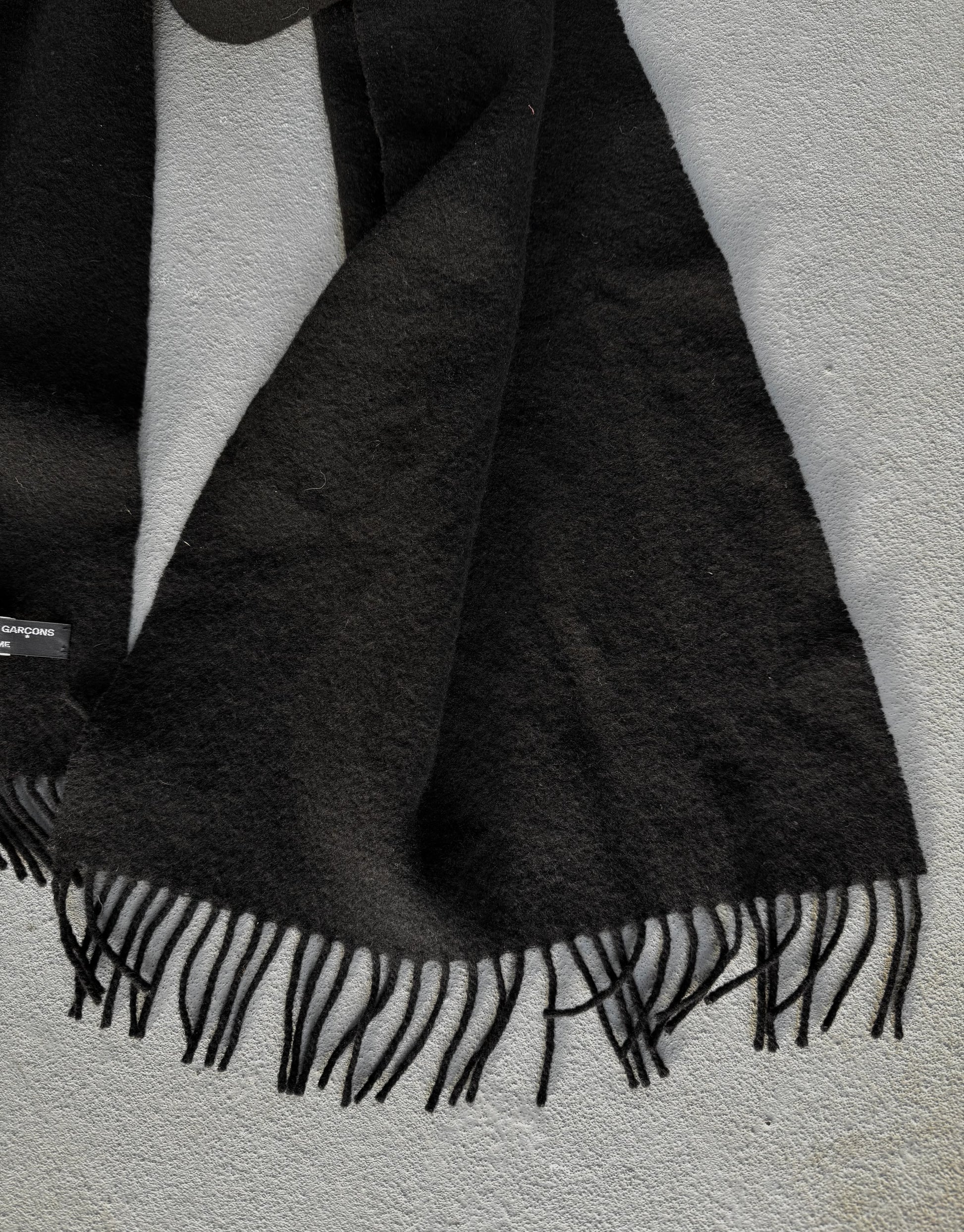 Black scarf with fringes draped over a white surface