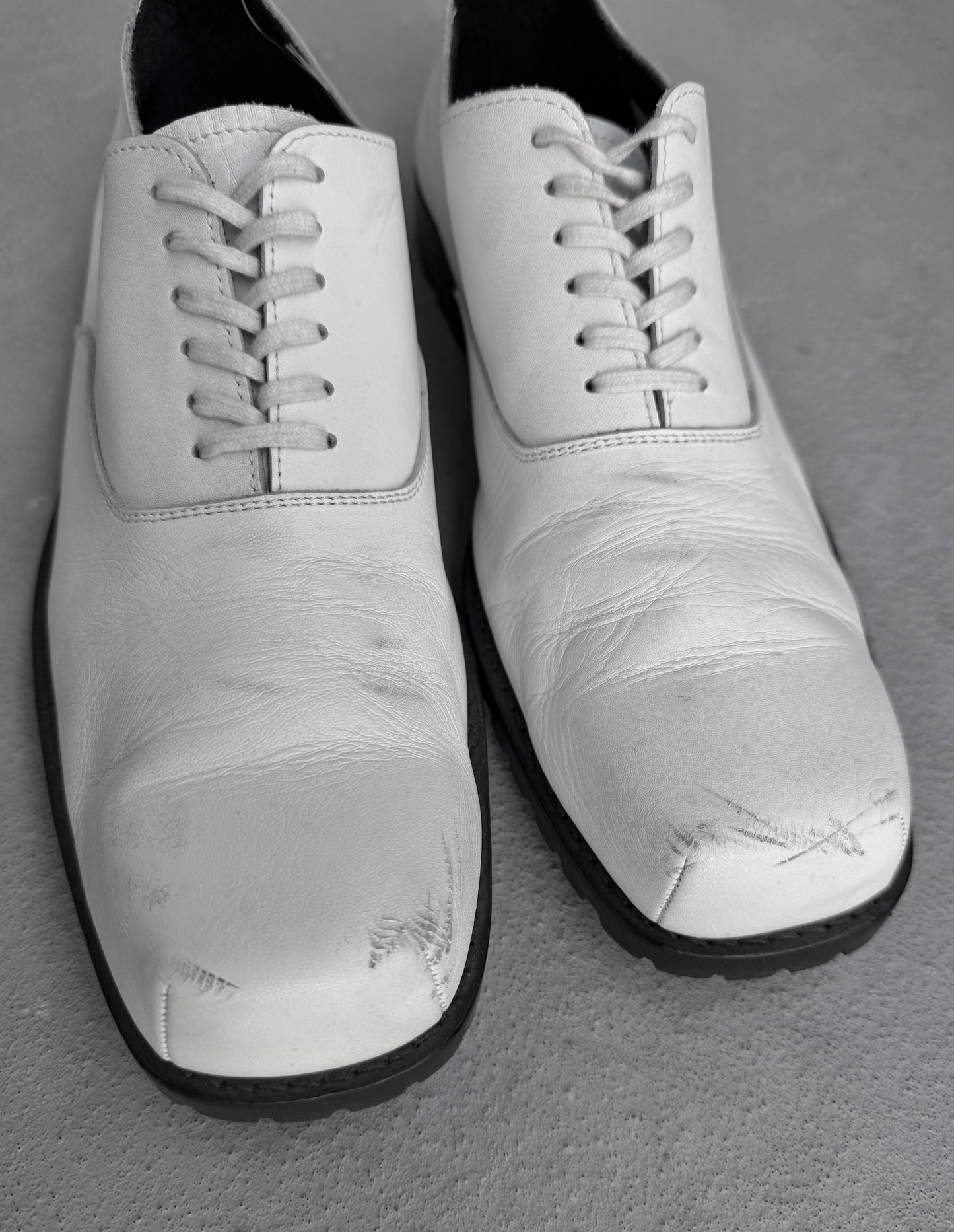 Pair of white shoes with black soles on a gray surface