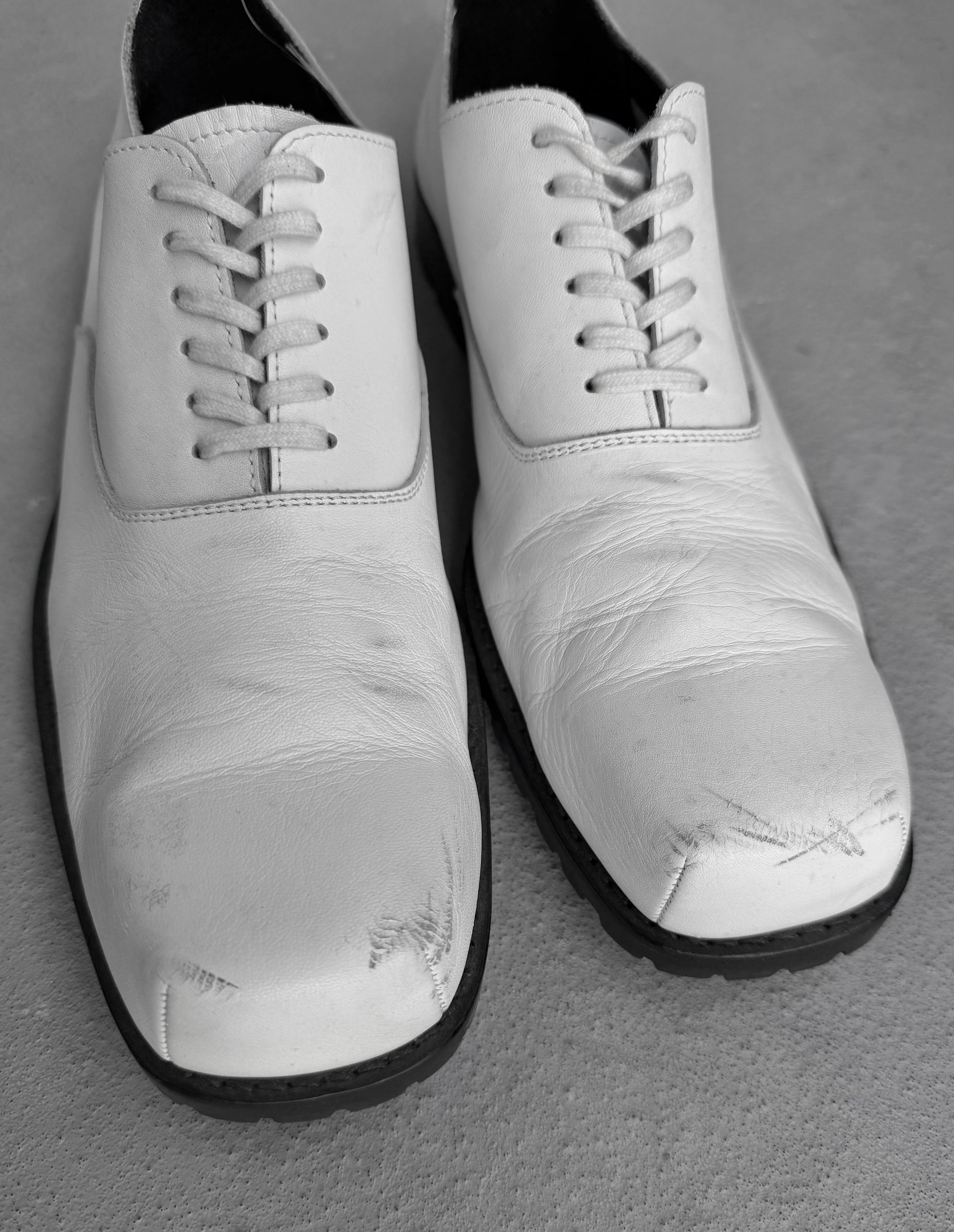 Pair of white shoes with black soles on a gray surface