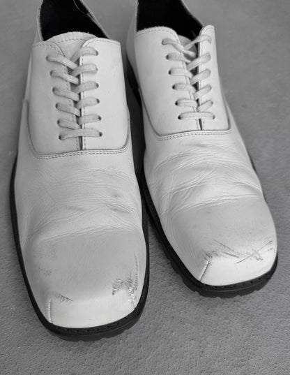 Pair of white shoes with black soles on a gray surface