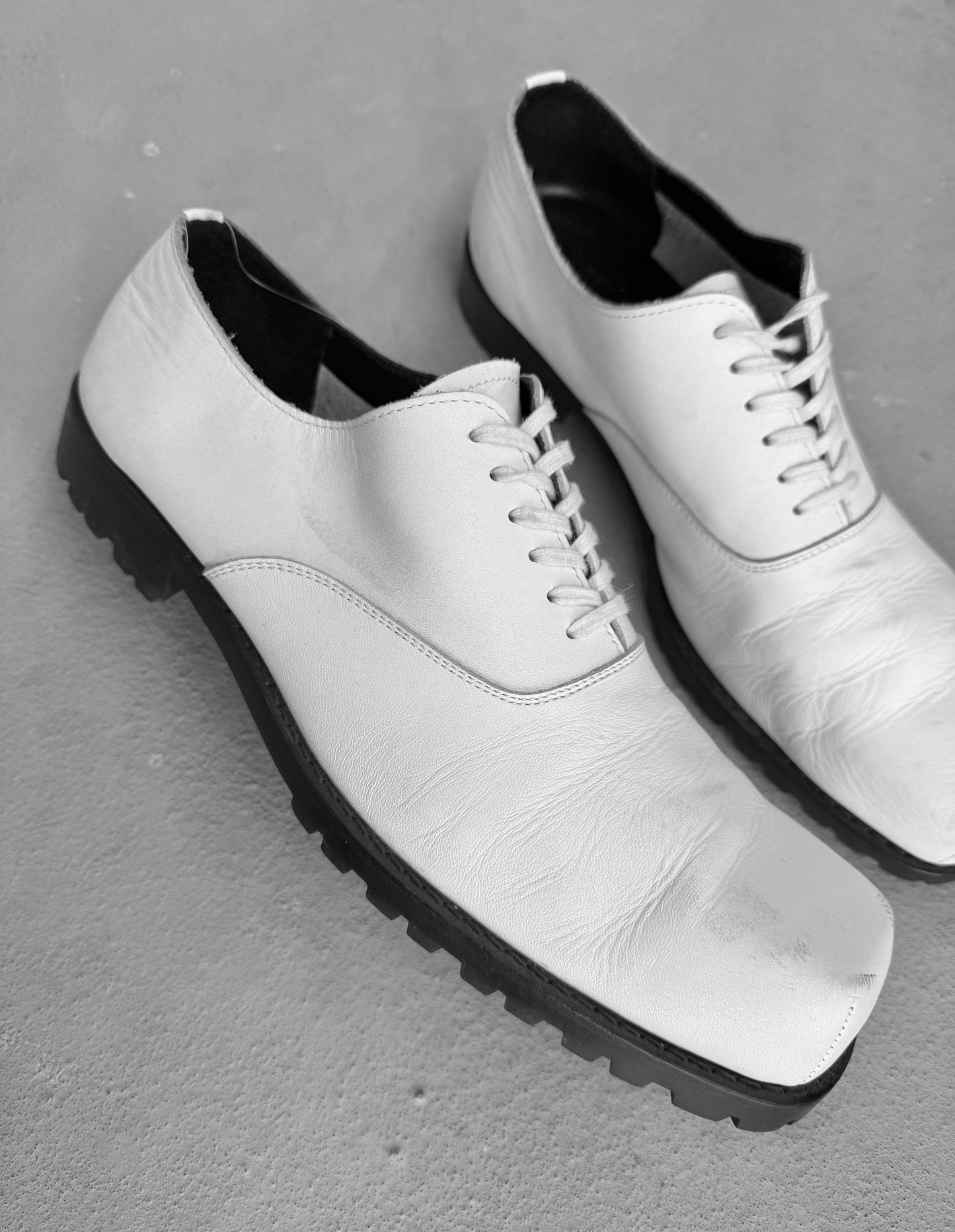 White leather shoes with black soles on a gray surface