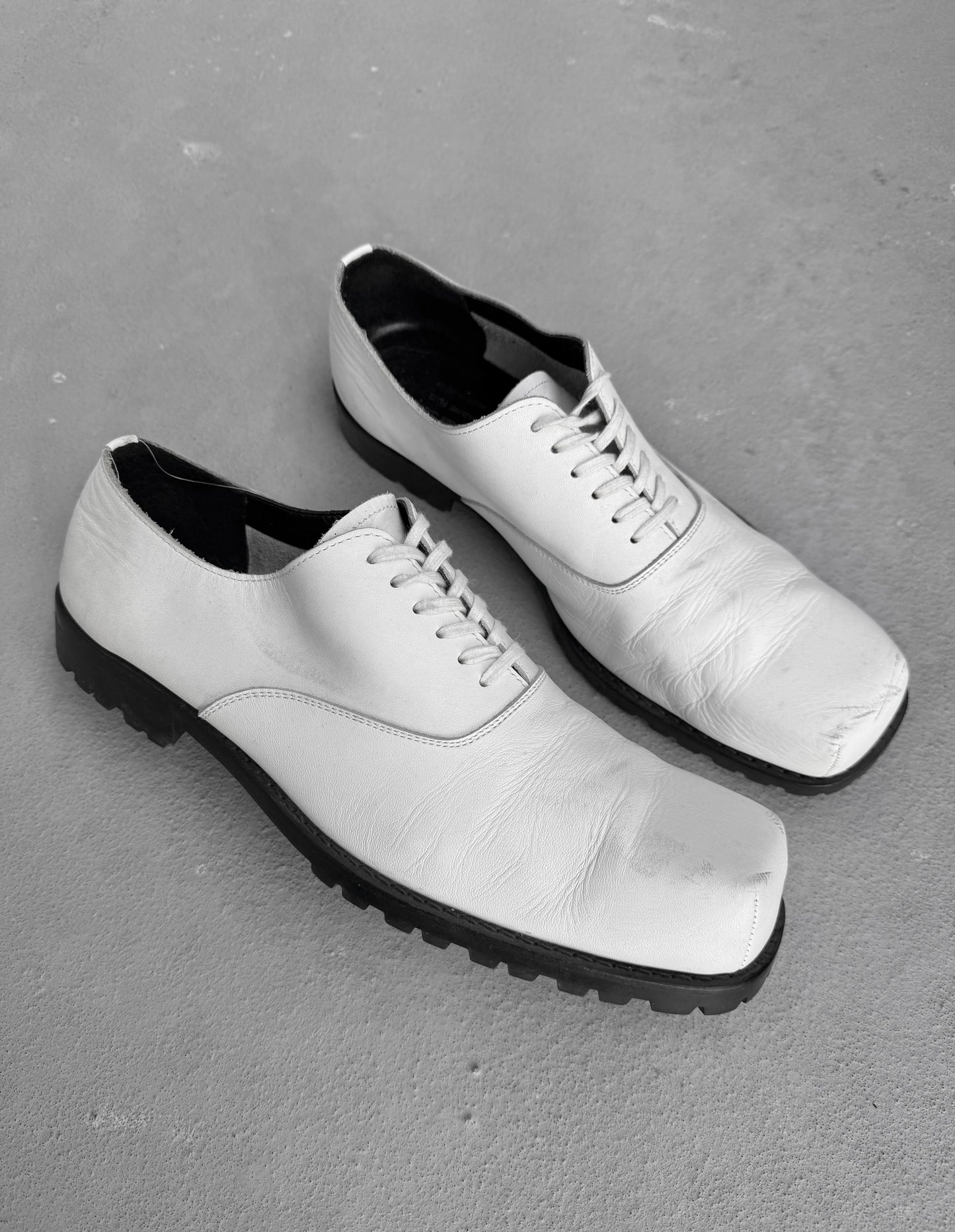 Pair of white leather shoes with black soles on a gray surface