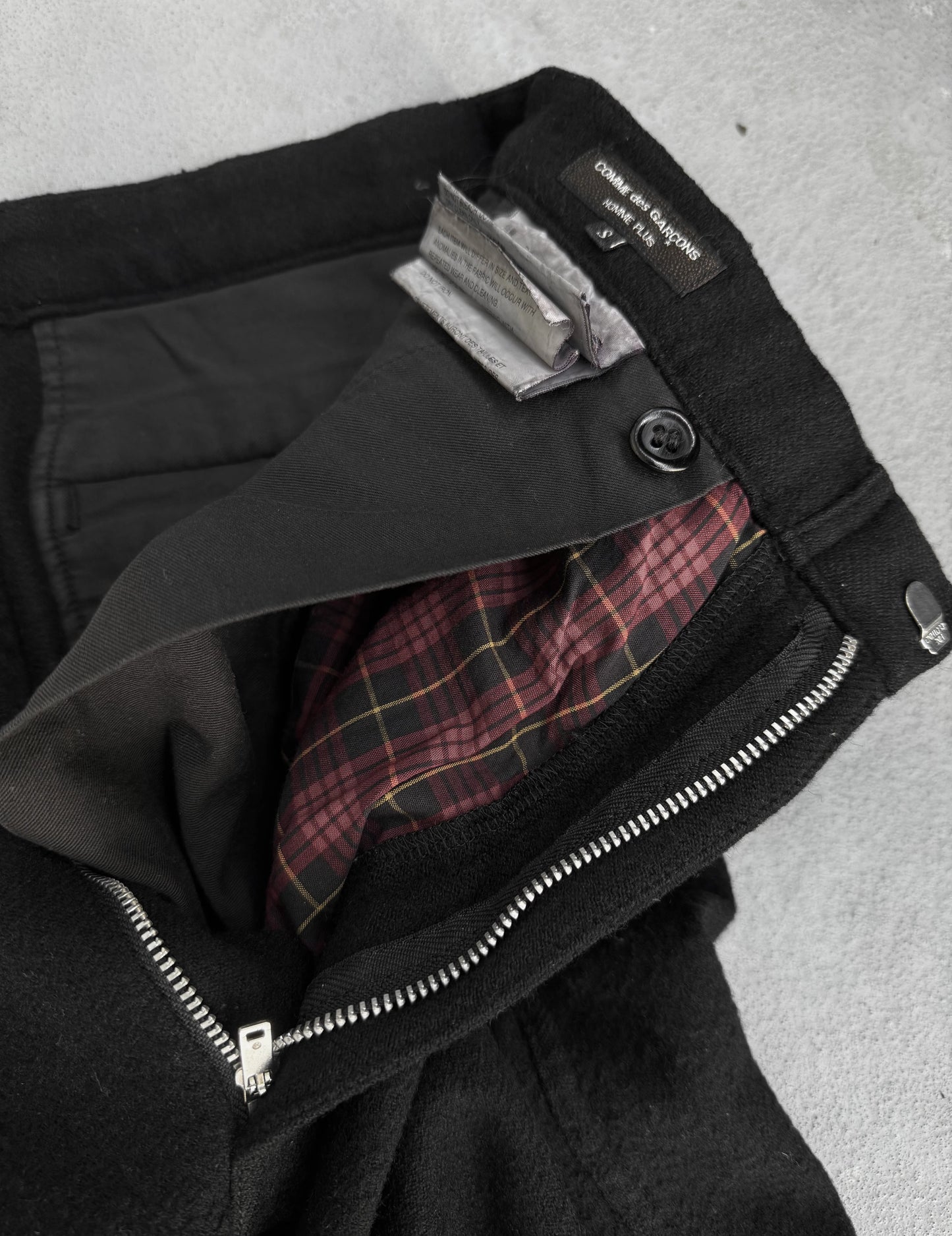 Close-up of a black jacket with plaid lining and visible brand label on a gray background
