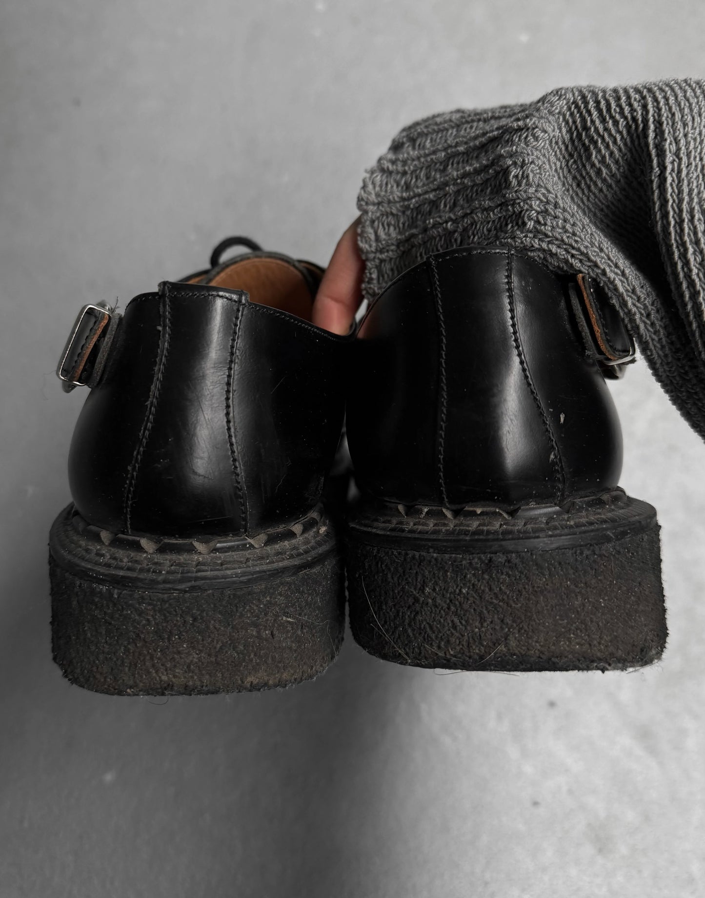 Black platform shoes with a thick sole held by a person wearing gray socks.