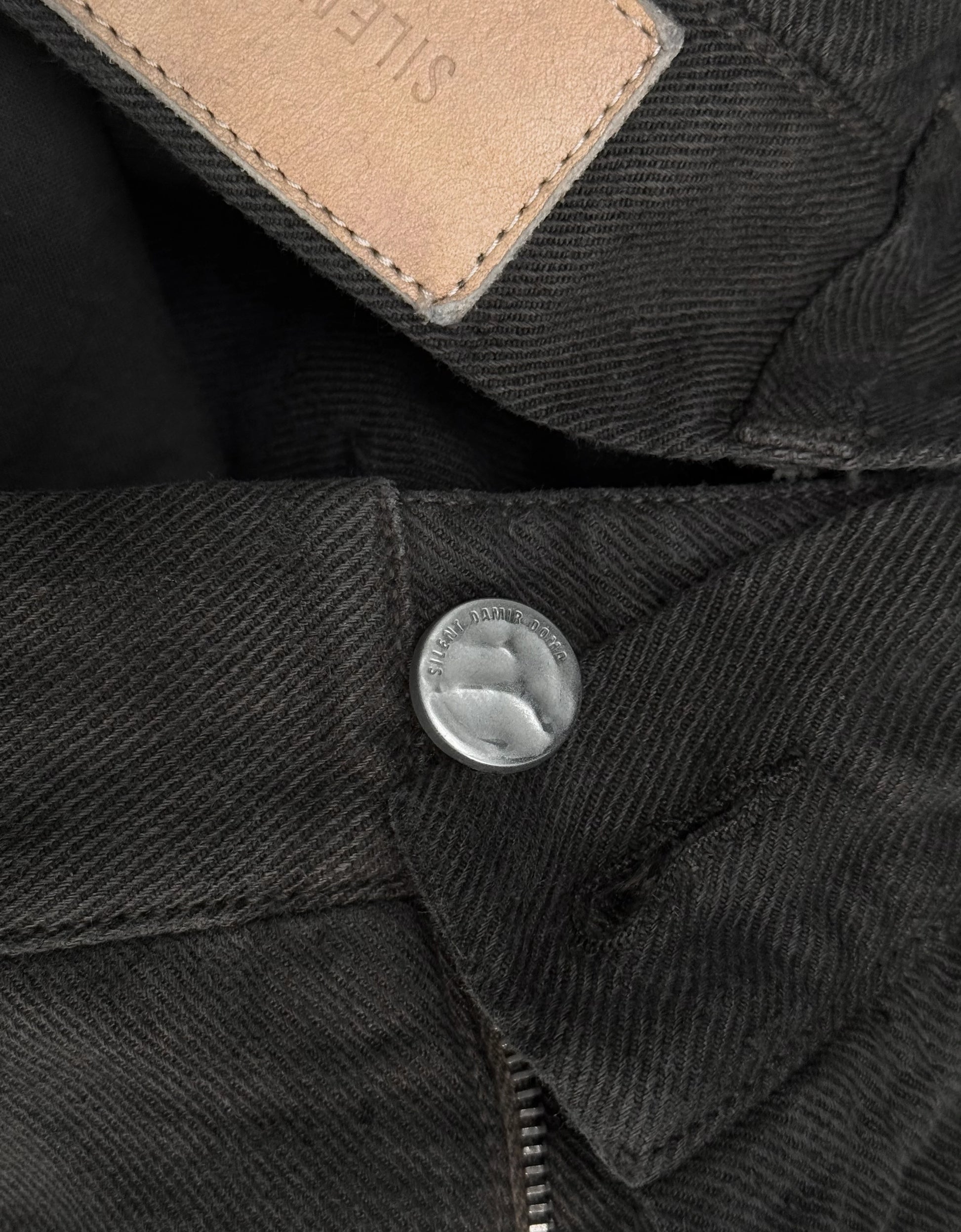 Close-up of a black denim jacket with a button and brand label.
