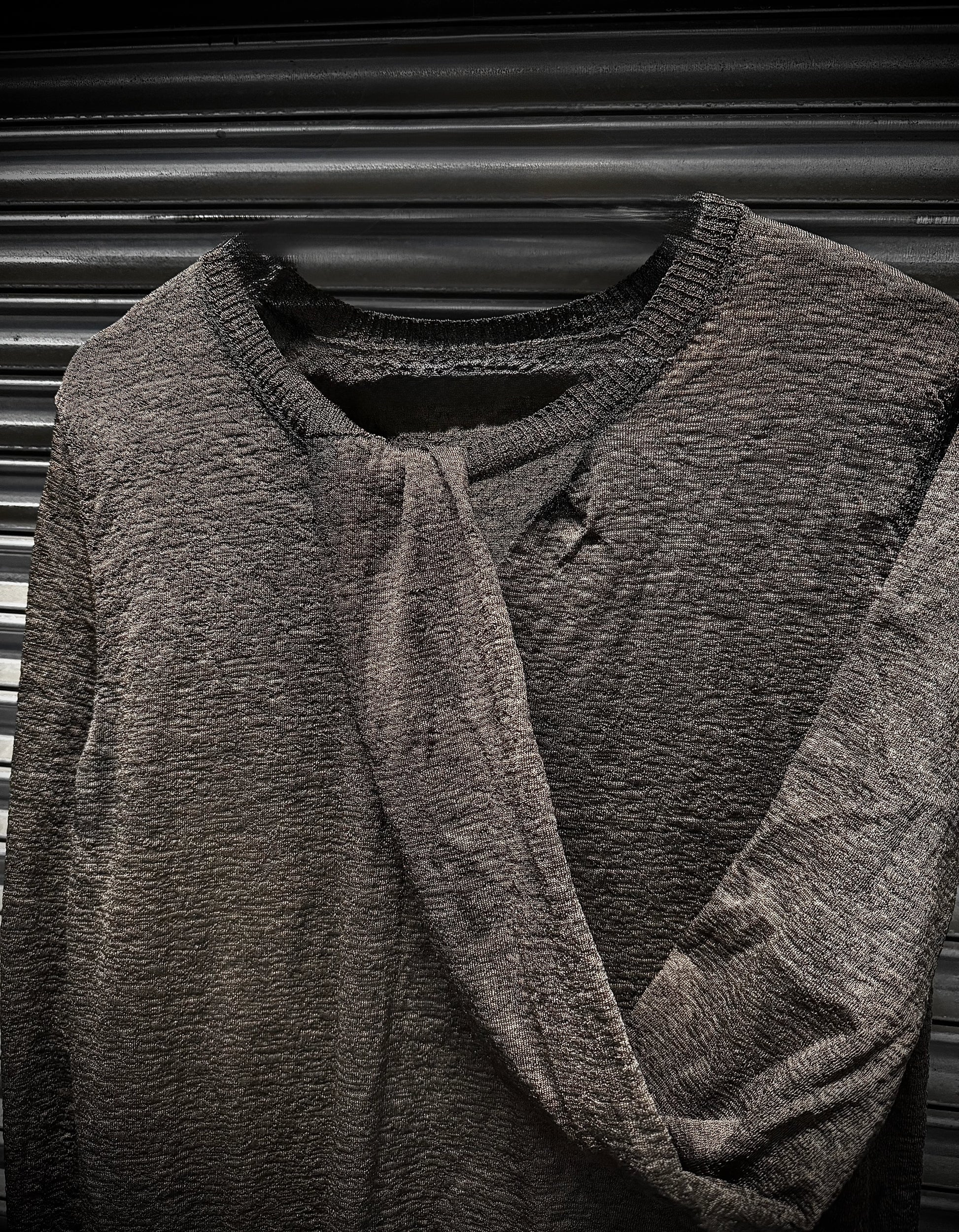Dark gray textured sweater on a hanger against a black background