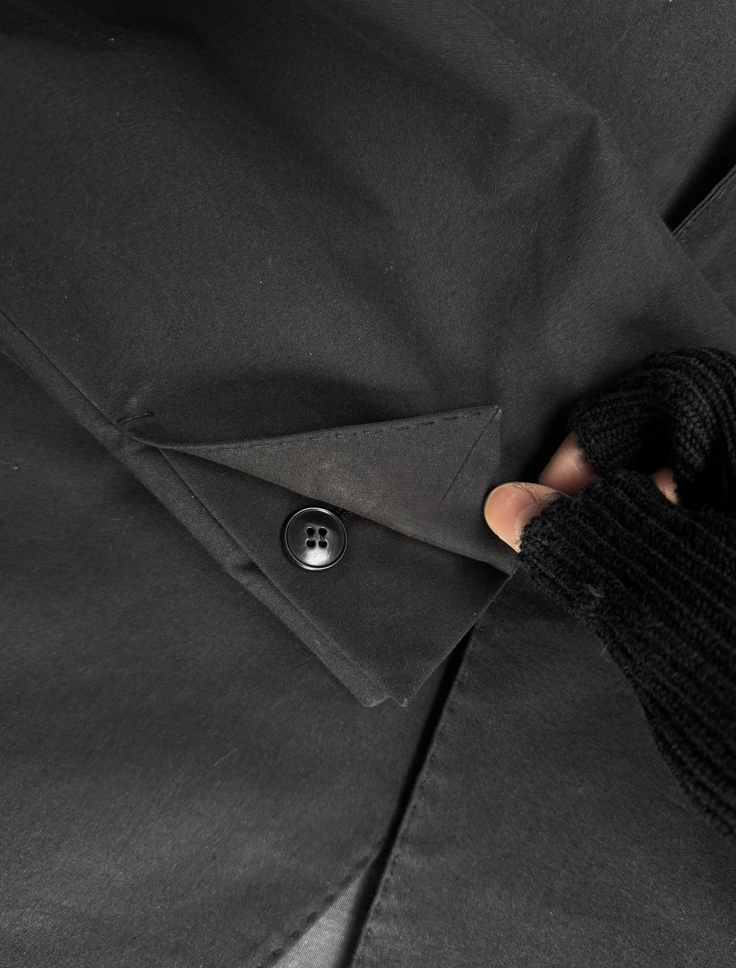 Close-up of a black coat with a button being adjusted by a hand wearing a textured glove.