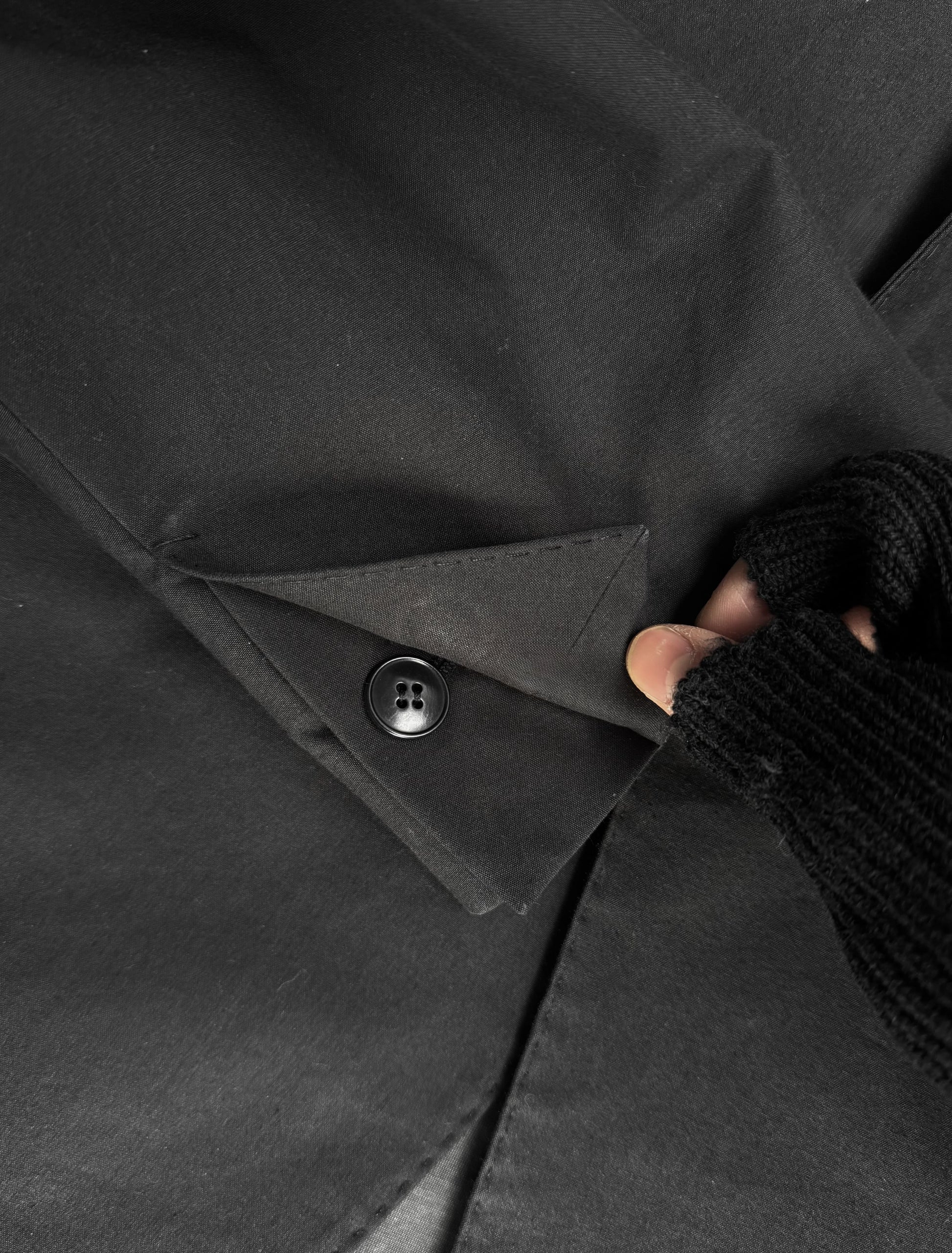 Close-up of a black coat with a button being adjusted by a hand wearing a textured glove.